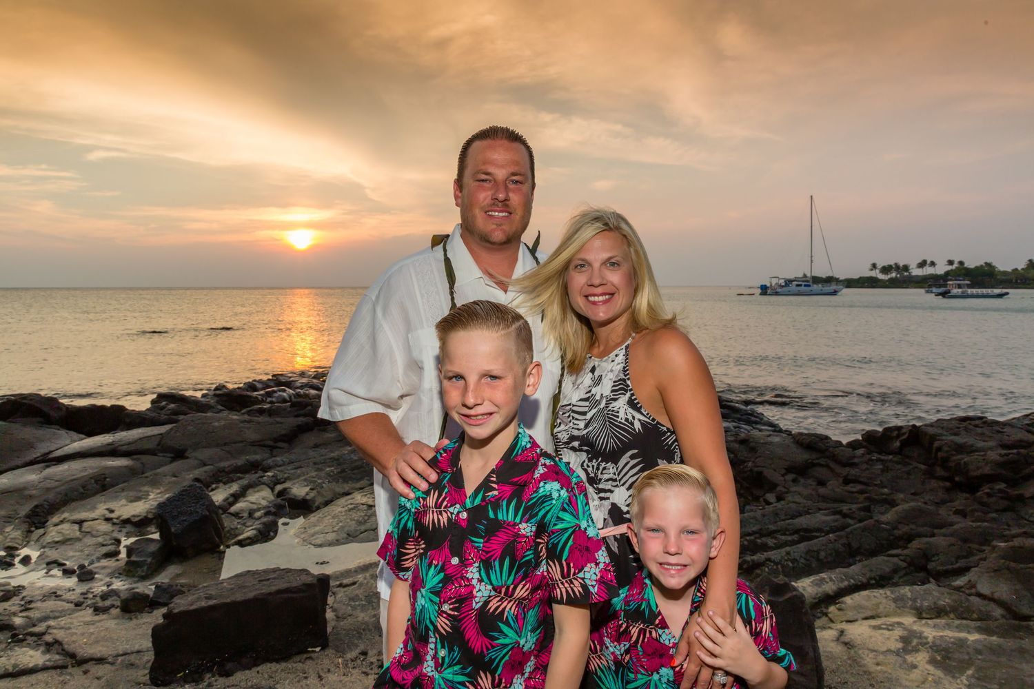 Family portrait on rocky beach during golden hour sunset with boats in background at the Old Airport Beach Park in Kailua Kona, Hawaii