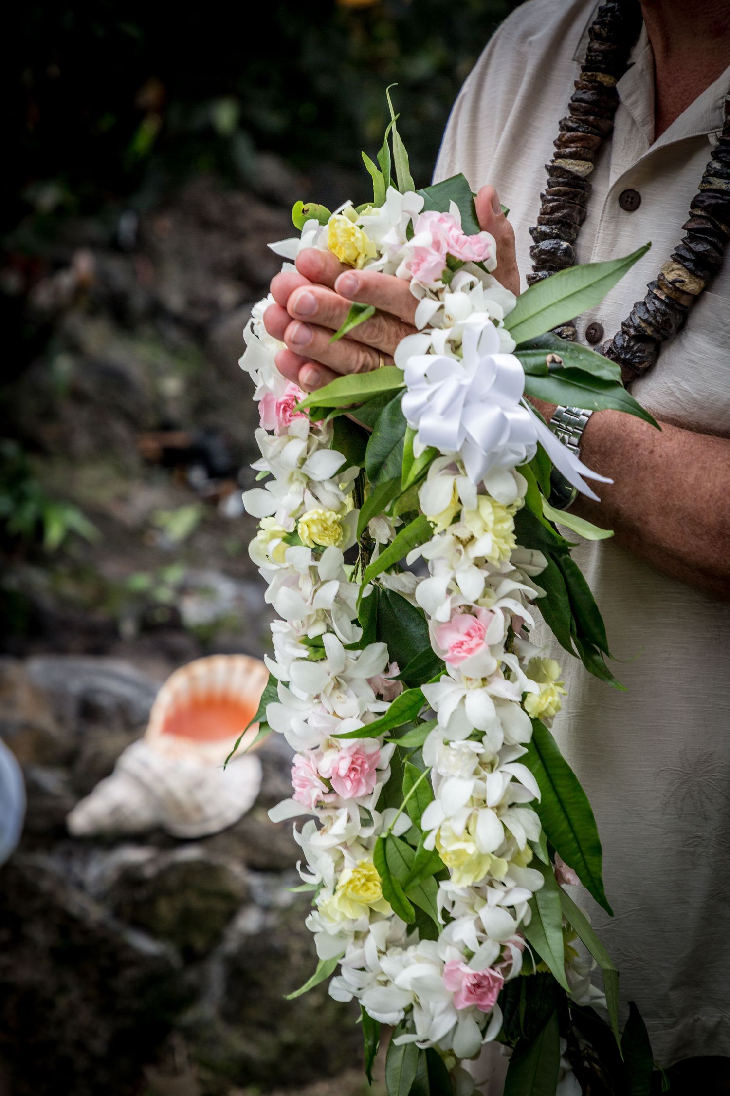 In a wedding in Kona, a minister holds a beautiful white orchid and pink rose wedding lei.
