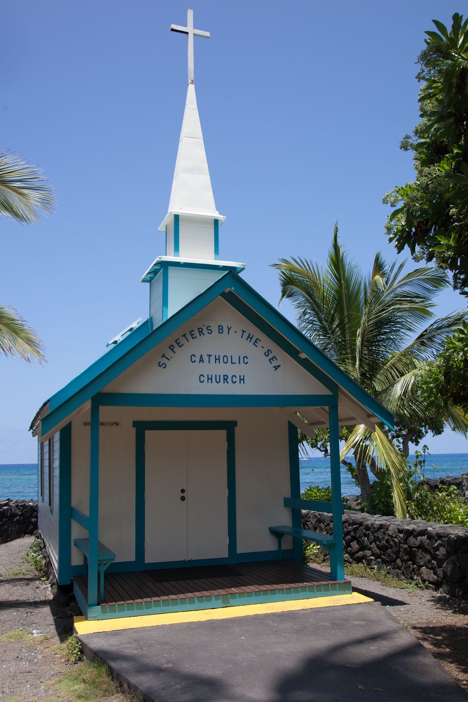 Small blue and white seaside Saint Peter Catholic chapel with cross and palm trees in Kailua Kona.