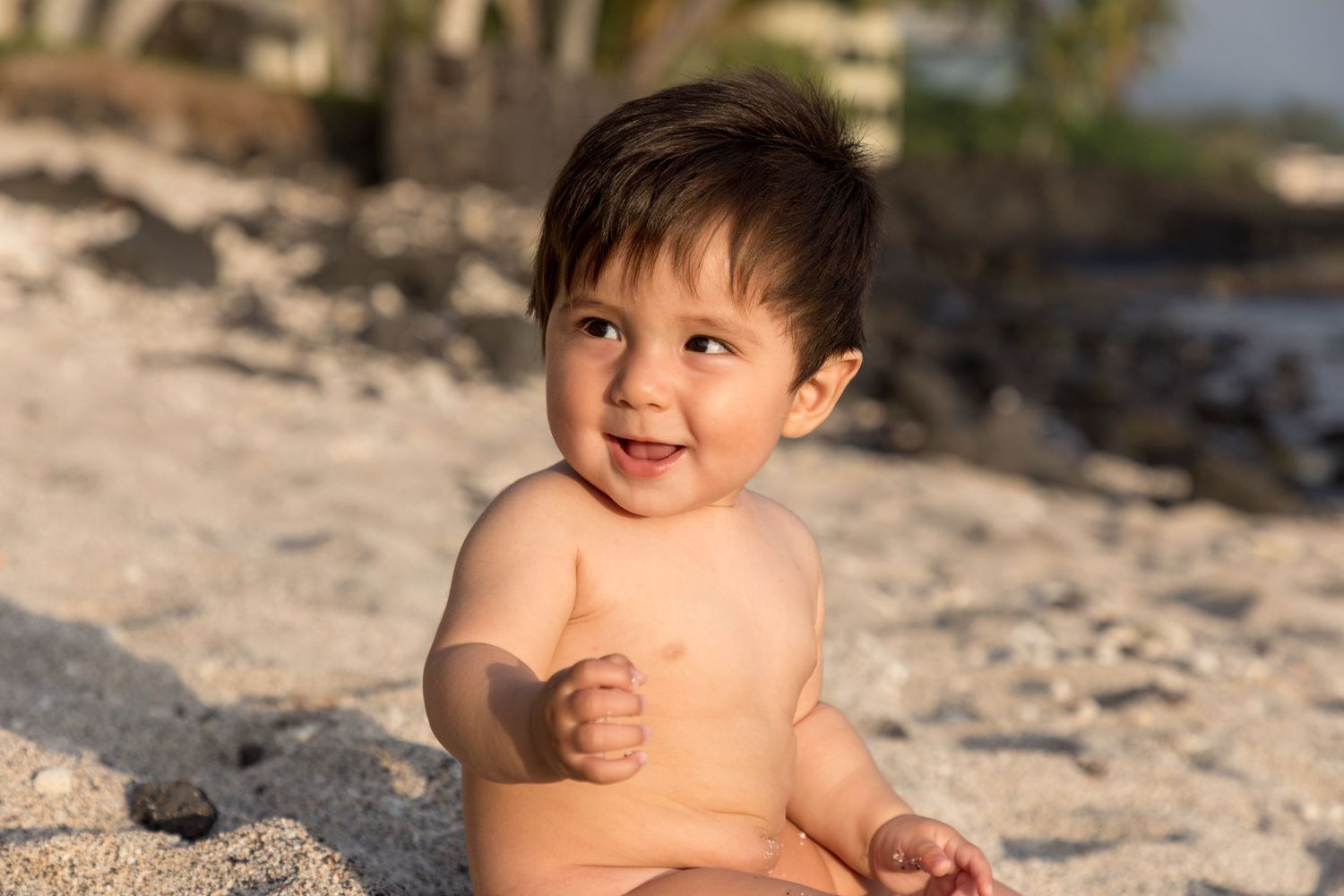 Smiling toddler plays on sandy beach during a sunny day at a beach on Ali'i drive near Kailua Kona, Hawaii..