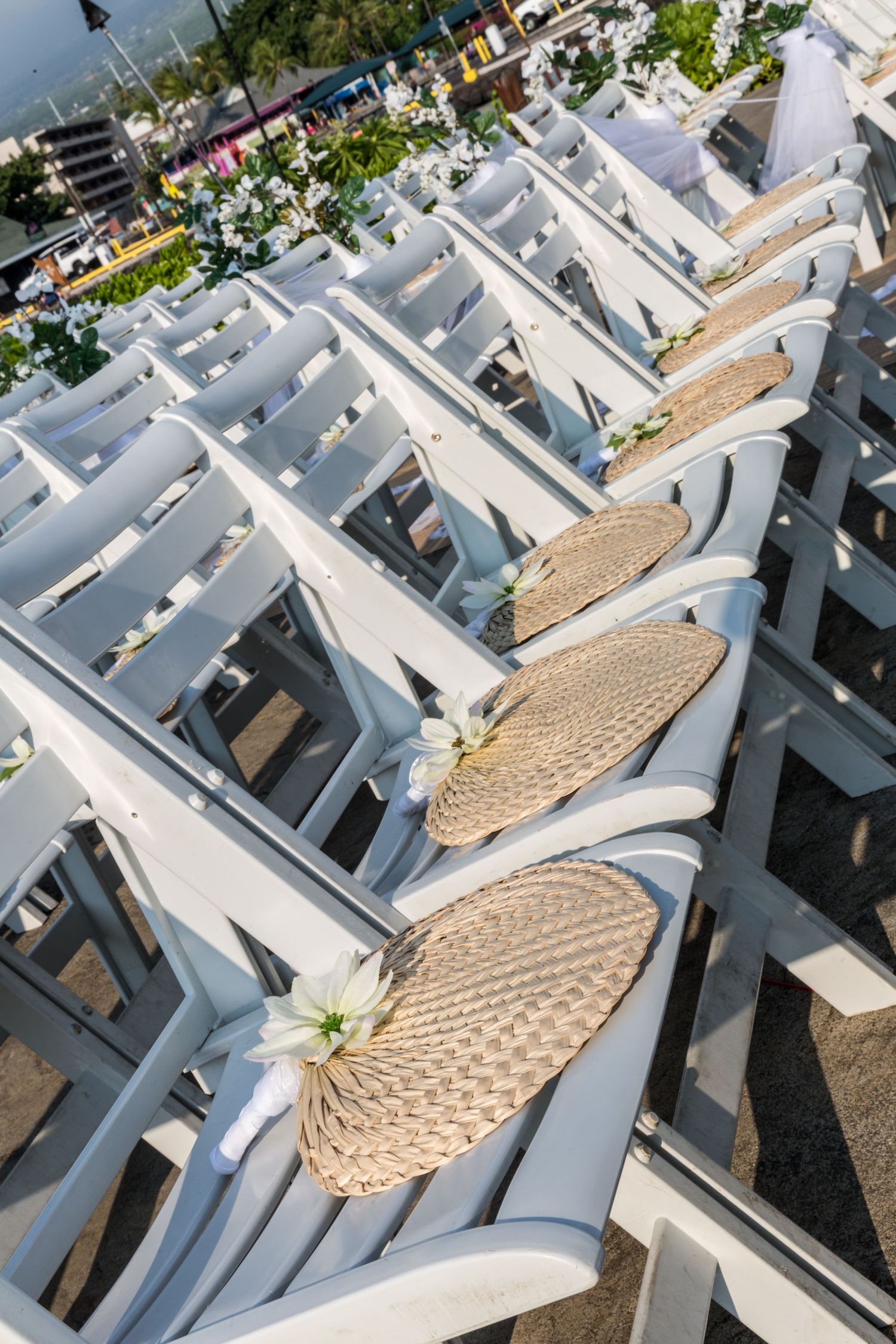 Rows of white wedding ceremony chairs with woven fans arranged outdoors at the King Kamehameha hotel in Kailua Kona, Hawaii.