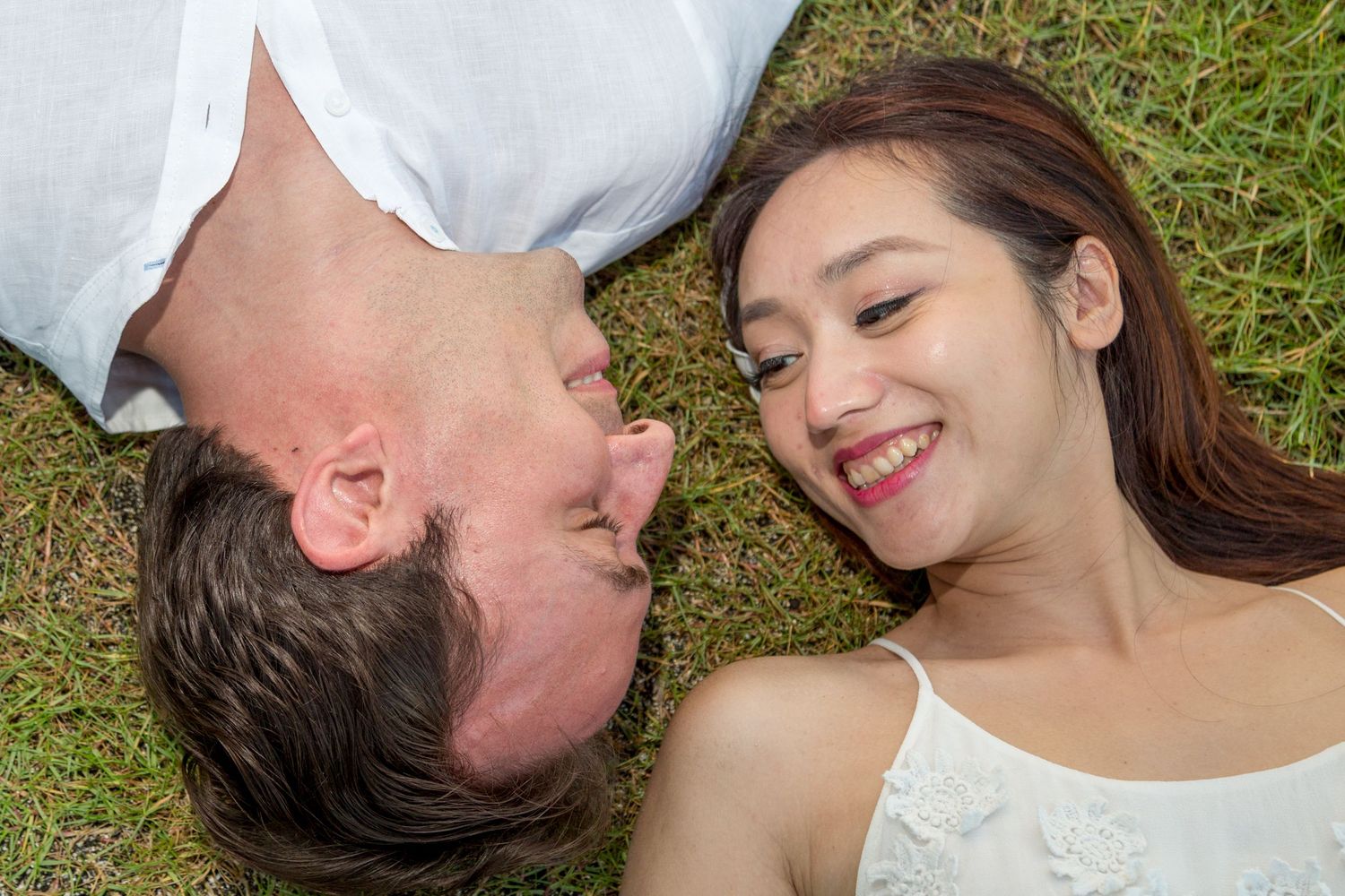 Couple lying on grass taking playful overhead portrait shot together during engagement session in Kailua-Kona Hawaii.