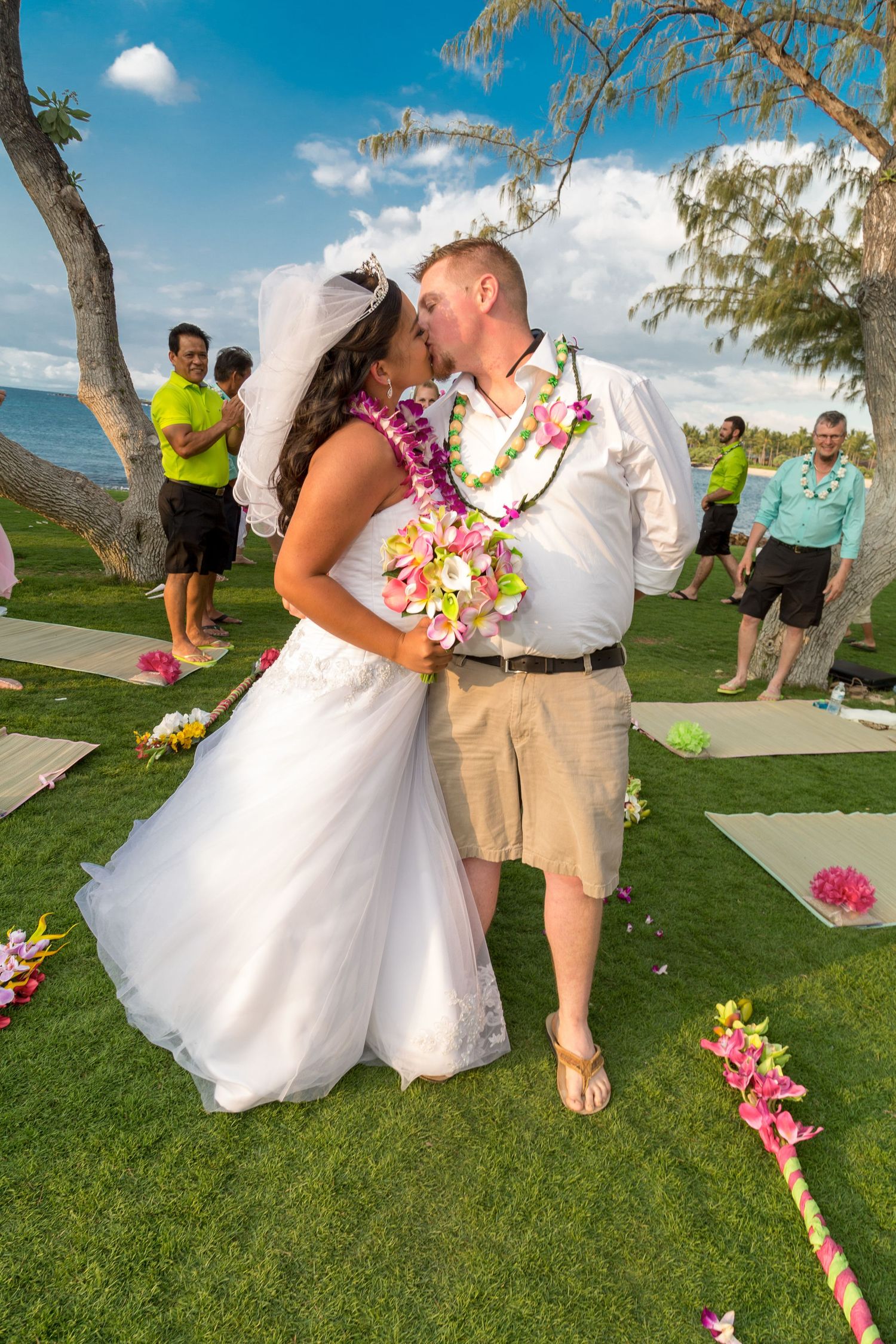 A couple shares a kiss during their beach wedding ceremony with tropical flowers and ocean views at Kikaua Point Beach Park in Kailua-Kona.