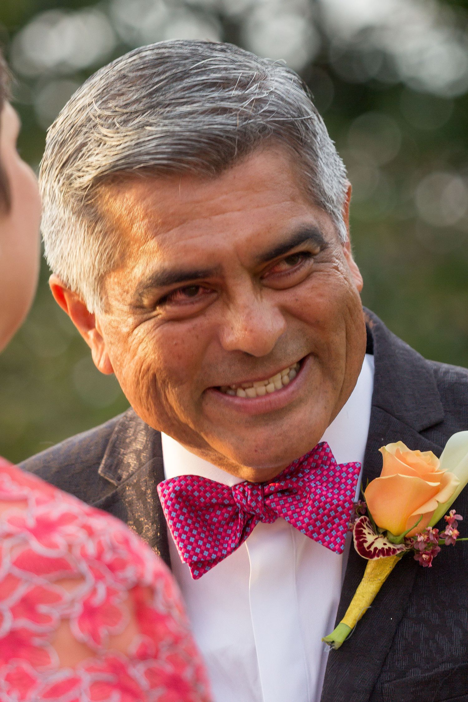 A portrait of a groom in a dark suit and pink bow tie with an orange boutonniere at a wedding in Captain Cook, near Kailua Kona.