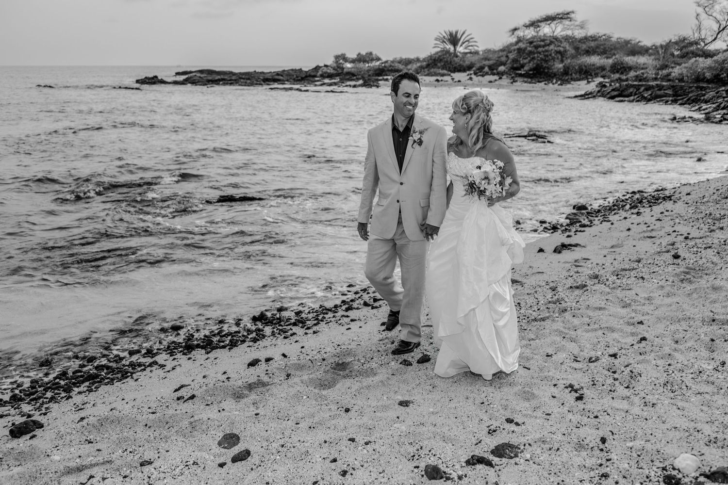 A black and white beach wedding portrait with waves crashing on rocky shoreline at the old airport Beach Park of Kailua Kona, Hawaii..