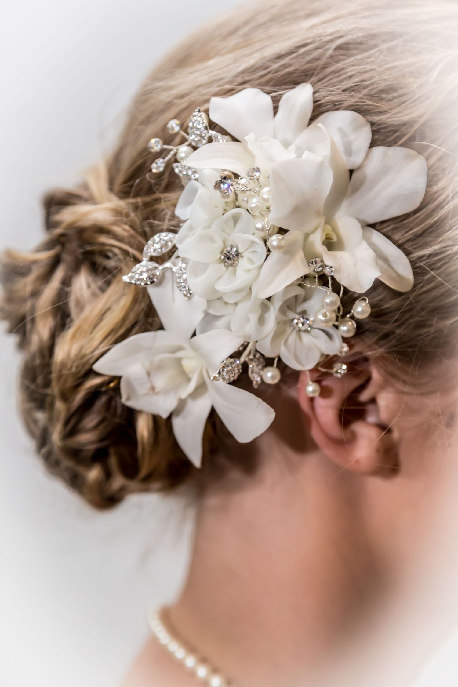 Elegant bridal hair accessory with white orchids and crystal details in an updo hairstyle.