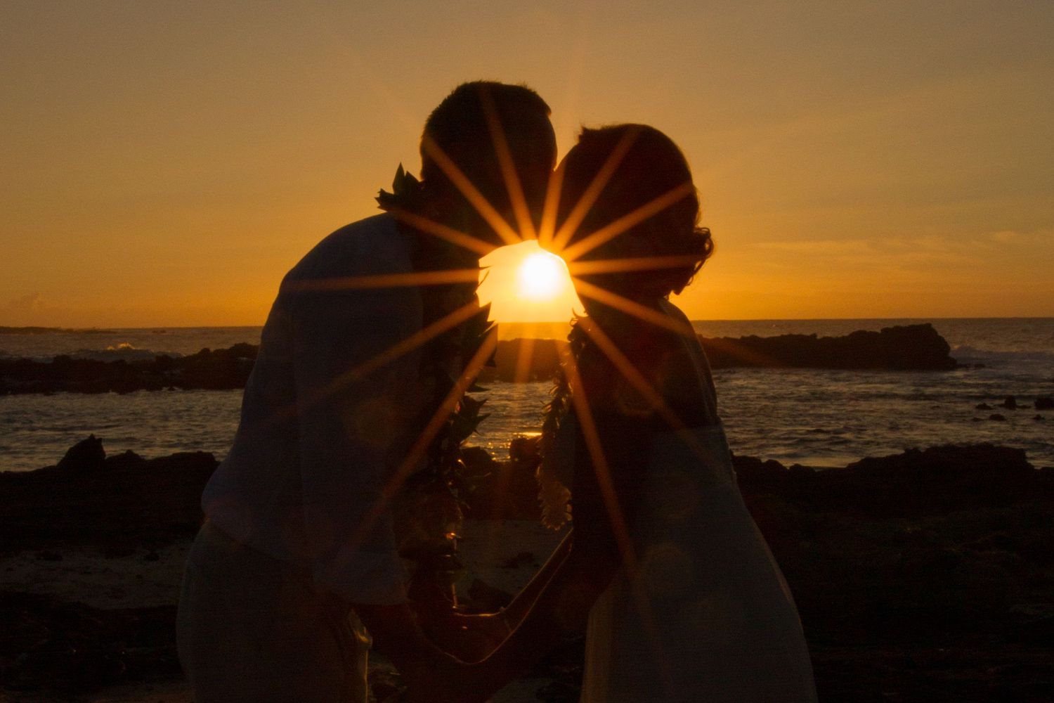 A silhouette of a couple kissing against the sunset with the sun rays creating a lens effect in Kailua Kona, Hawaii.