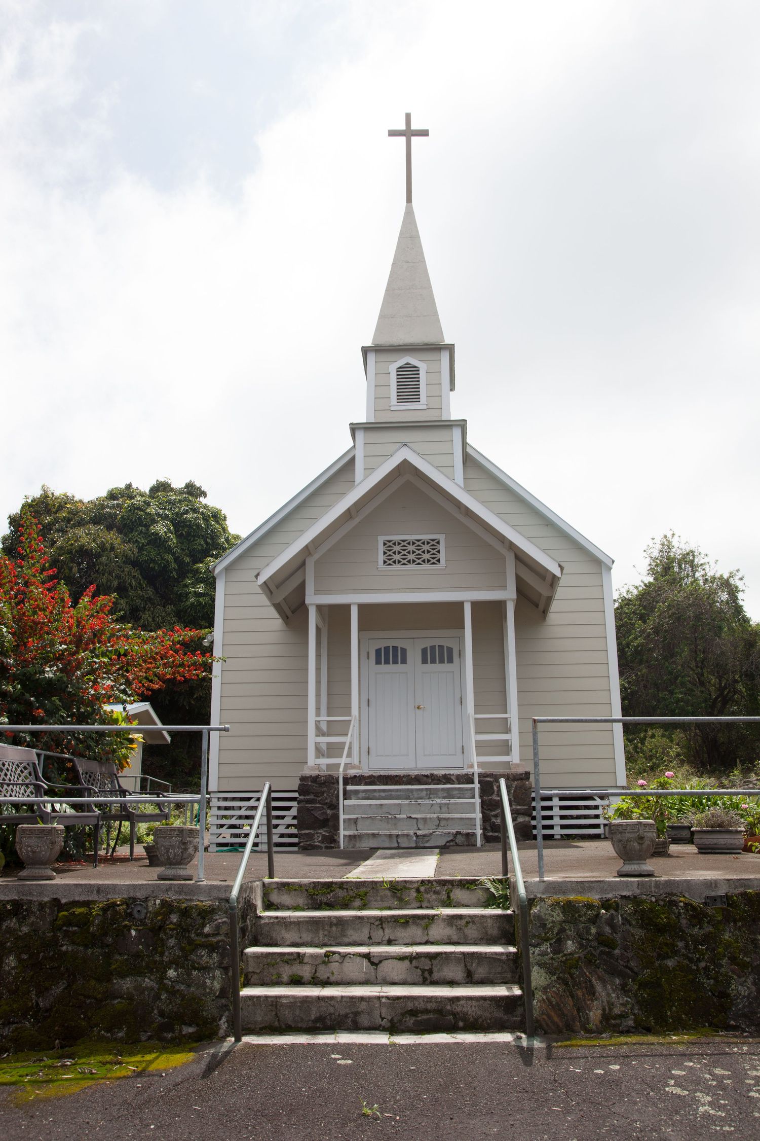 Small white wooden church with steeple and cross on top in rural setting.
