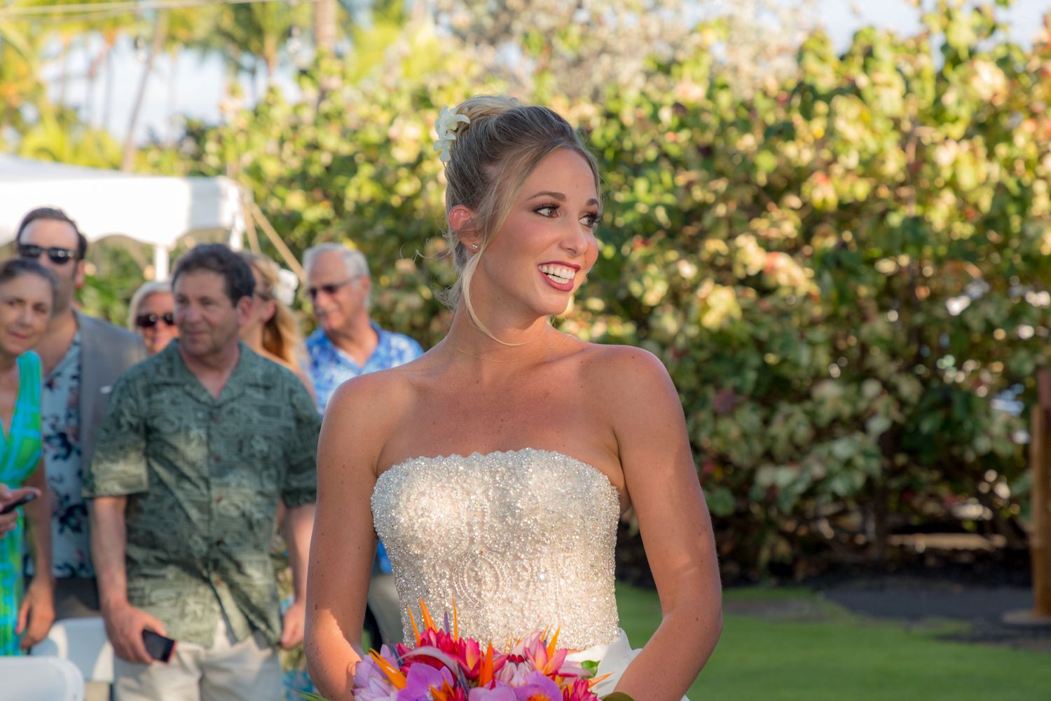 Wedding party celebrating outdoors in garden setting with greenery and formal attire on sunny day.