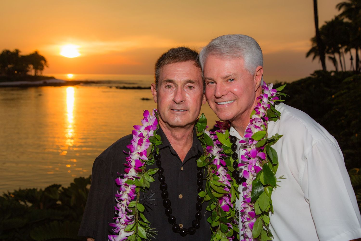 2 men wearing purple orchid leis pose together at sunset after a same sex wedding ceremony at the Hilton Waikoloa Village in the Big Island.