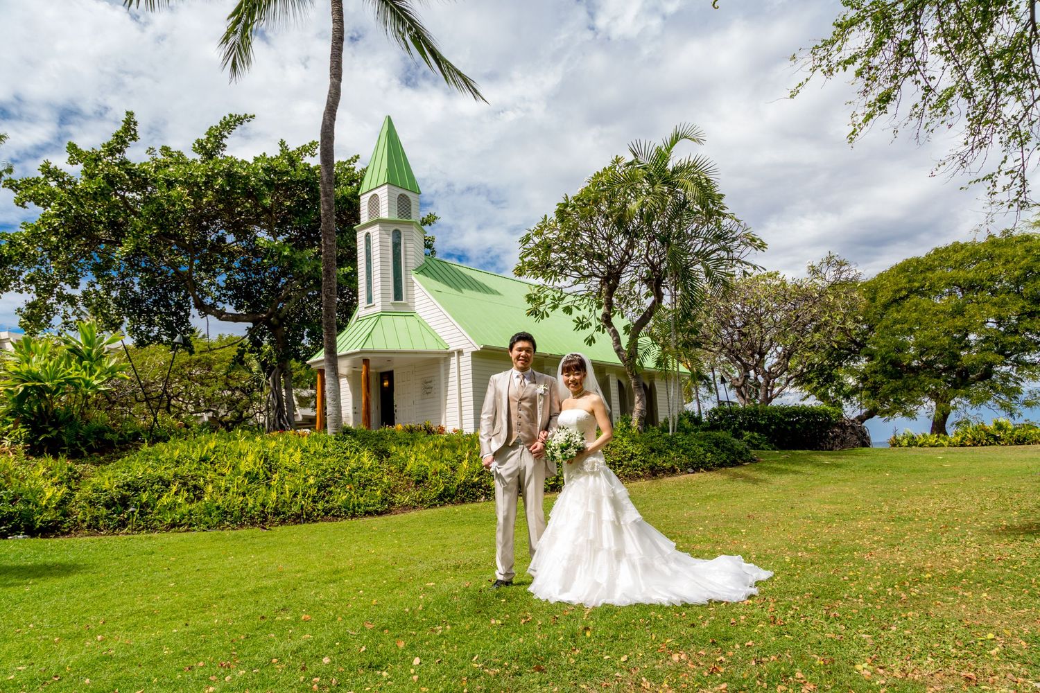 A couple poses in front of the charming green chapel of the Bayside Wedding Chapel of the Outrigger Kona Resort & Spa.