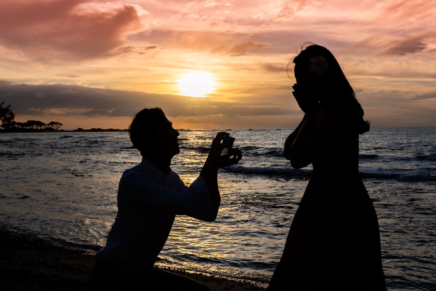 A silhouetted proposal scene against a dramatic sunset on Kukio Beach in Kailua Kona, Hawaii.