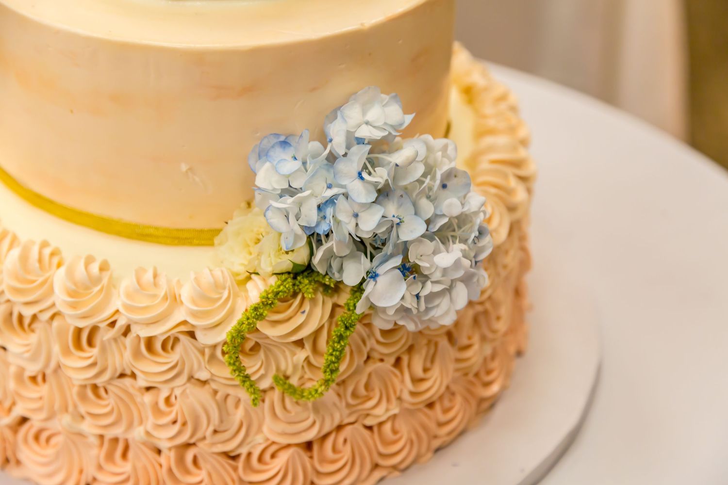 Wedding cake decorated with ombre rosettes and blue hydrangea flowers.
