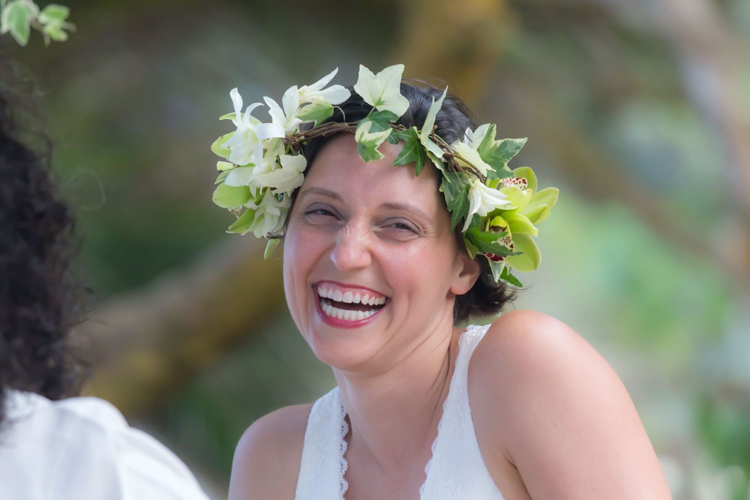 A laughing wedding bride wearing a floral crown outdoors at a same sex wedding in Kailua Kona, Hawaii.