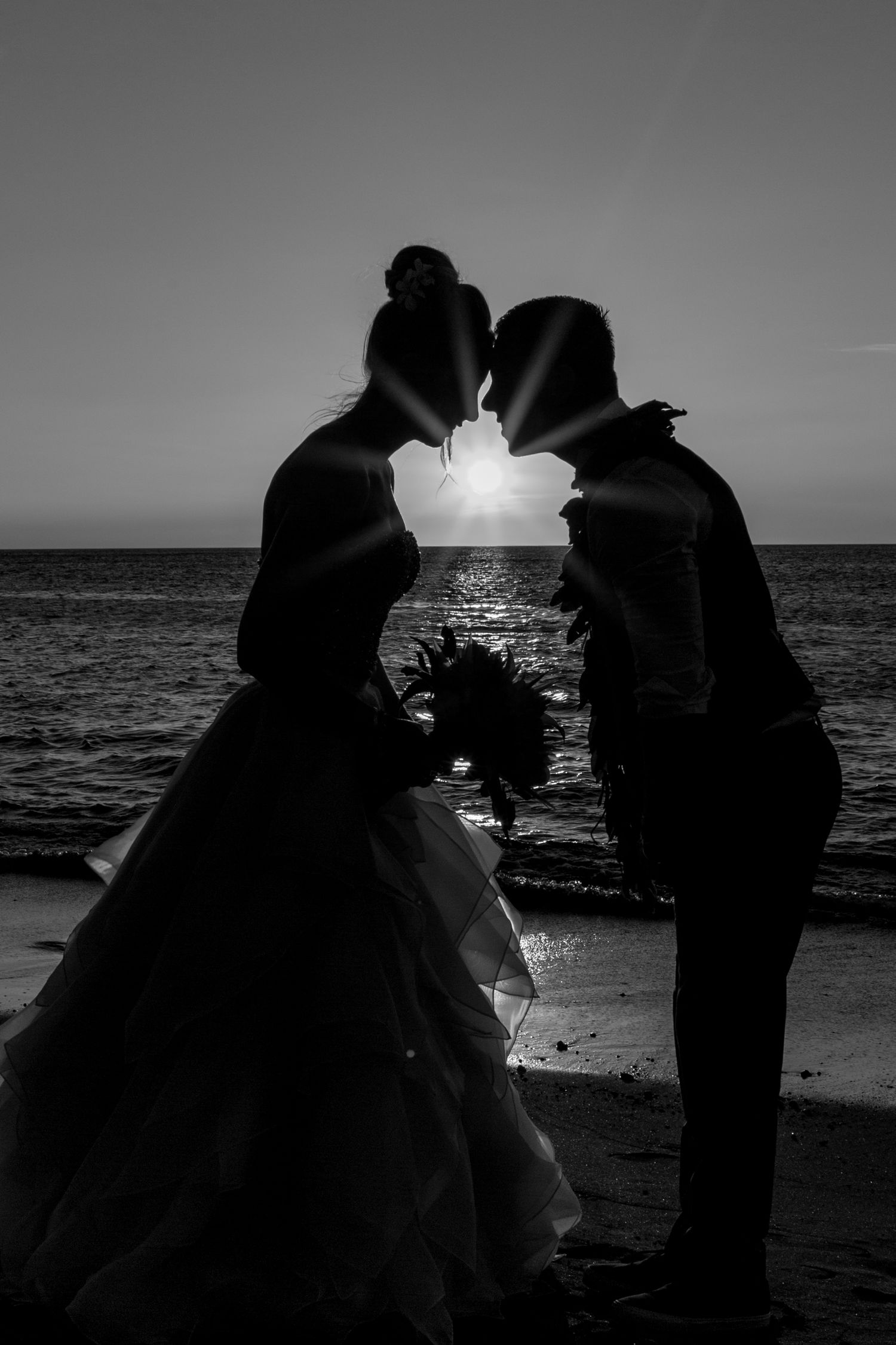 A romantic silhouette of a couple kissing at sunset on the beach with the sun perfectly positioned between them.