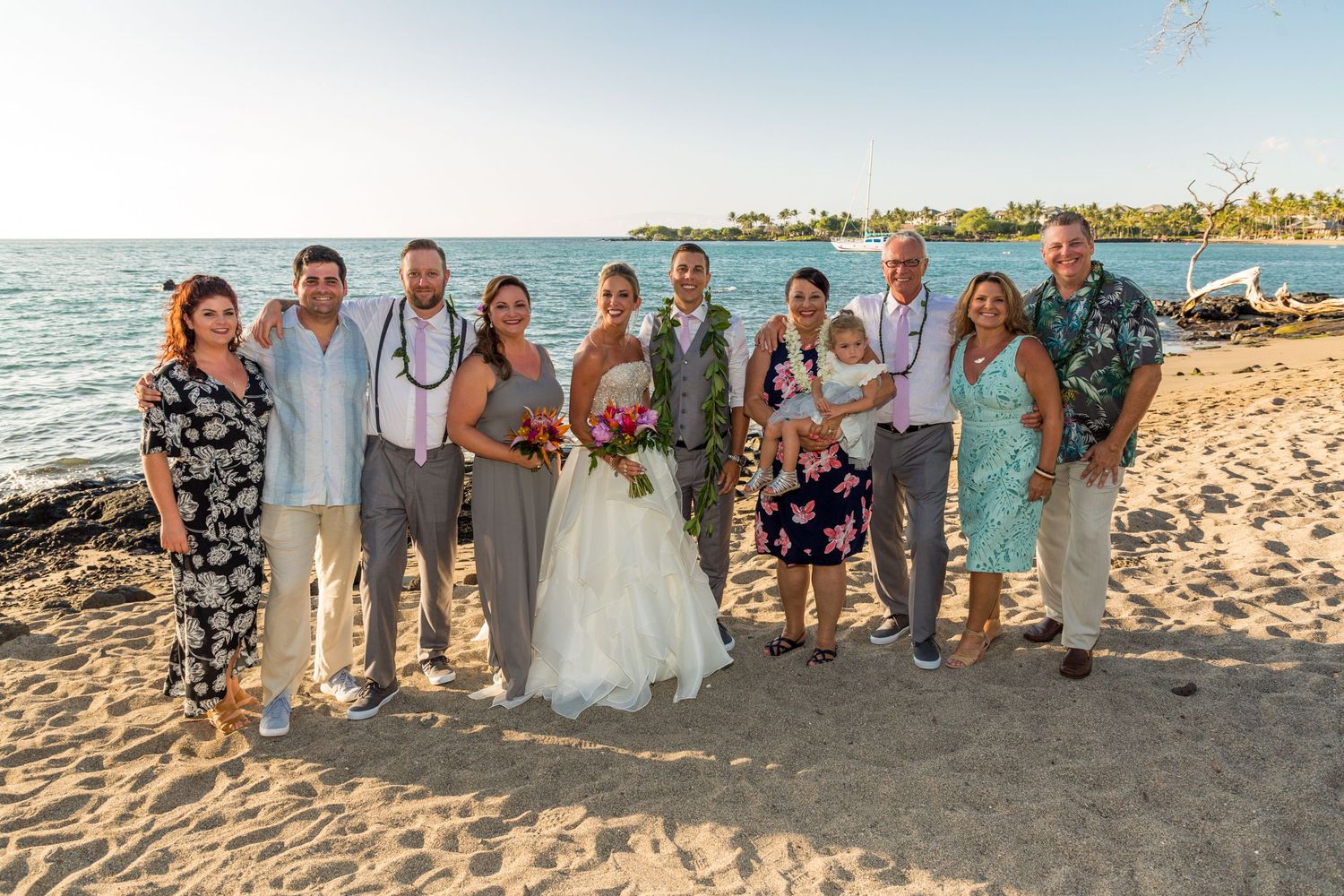 Wedding party poses together on a tropical beach at sunset with ocean waves and coastal houses in the background.