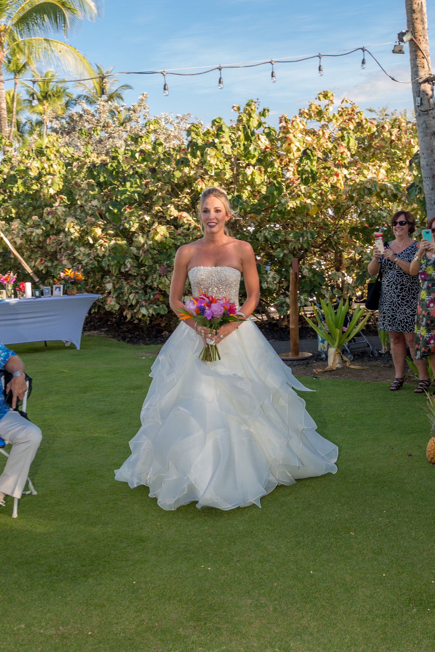 A beautiful outdoor garden wedding ceremony with string lights and palm trees in a tropical setting.