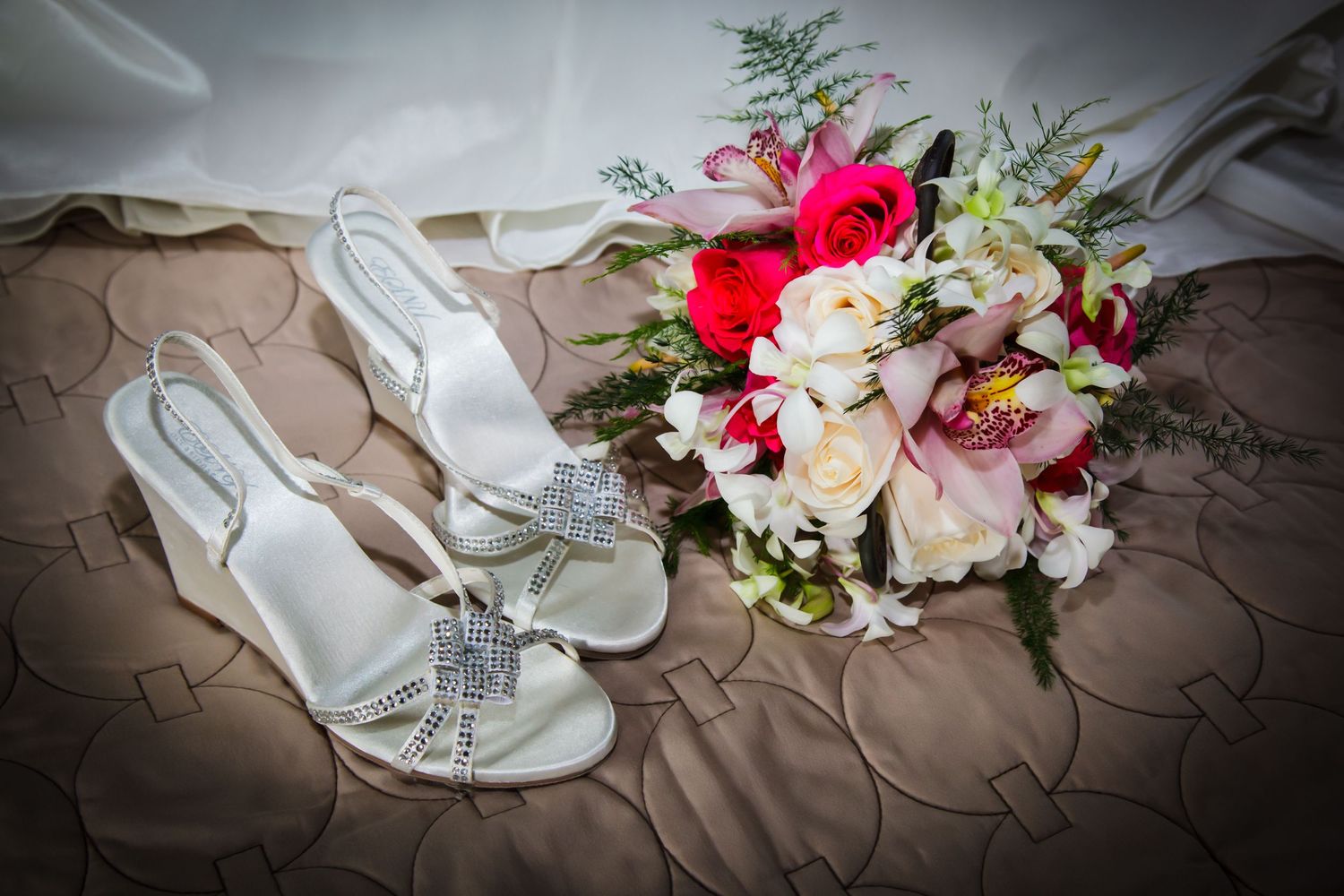 Elegant bridal bouquet with red and white flowers next to crystal-embellished wedding shoes.