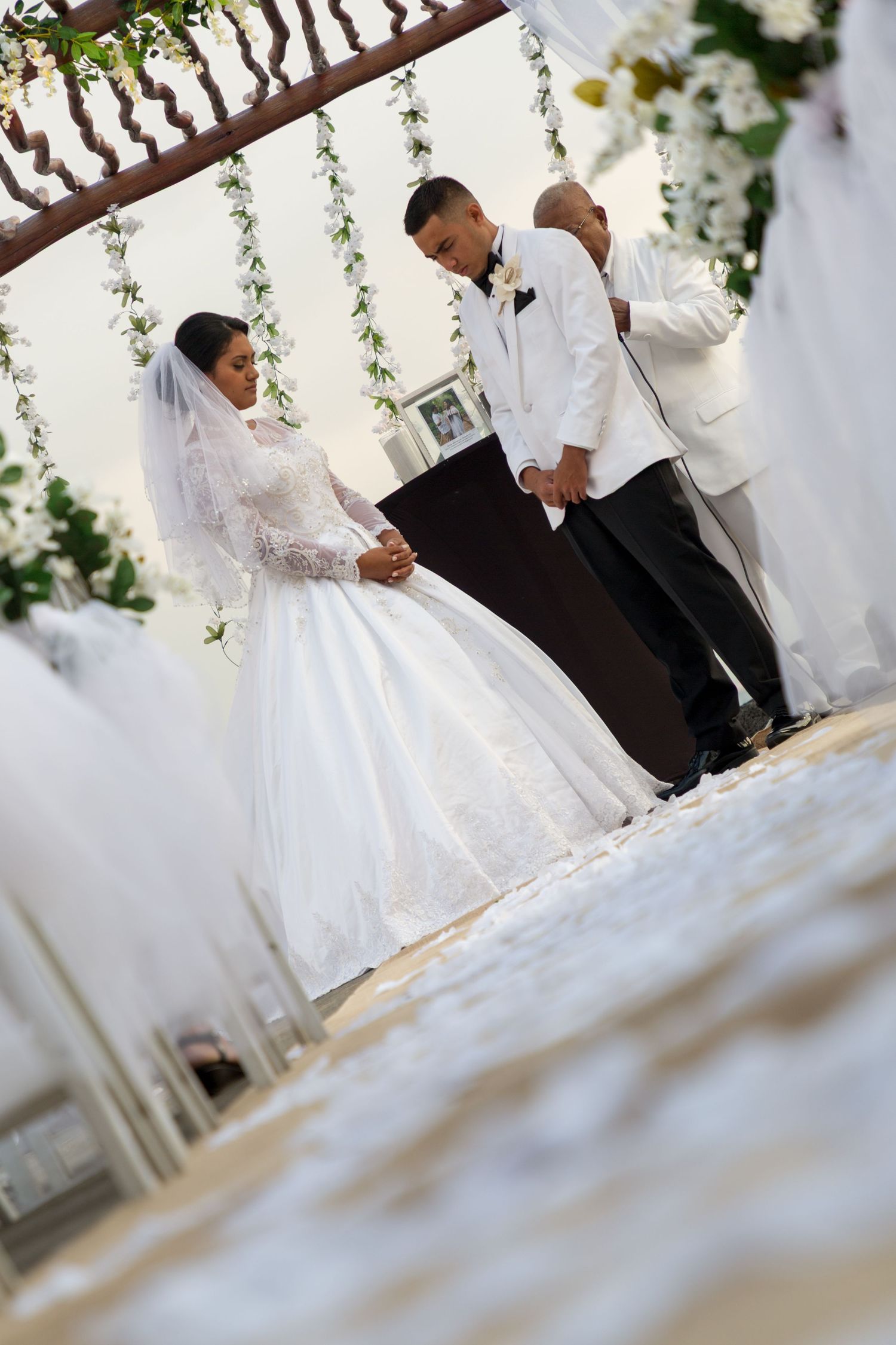 A romantic wedding ceremony with floral decor and hanging vines against a white backdrop at the Outrigger Resort and Spa in Kailua Kona.