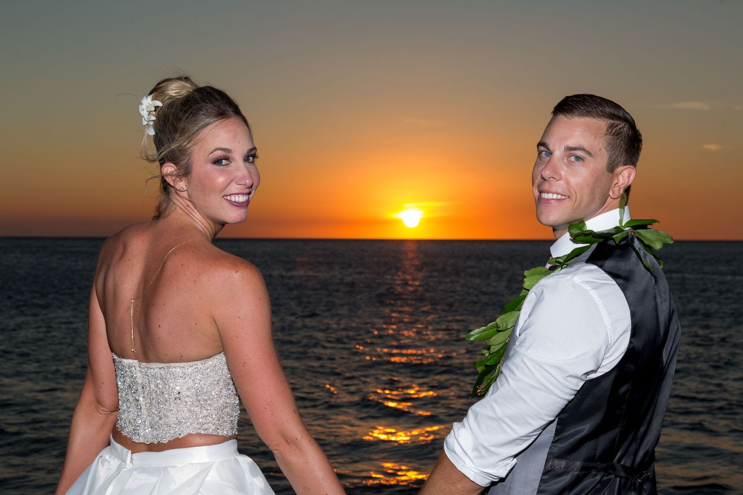 A couple looks back towards the photographer at a sunset on a beach near Kailua Kona, Hawaii.