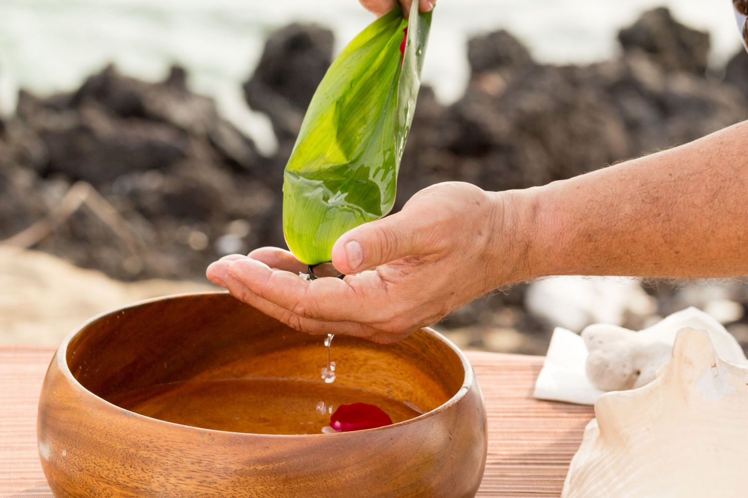 Water pours from green leaf into wooden ceremonial bowl during traditional wedding ritual in the Old Airport Beach Park in Kona, Hawaii.