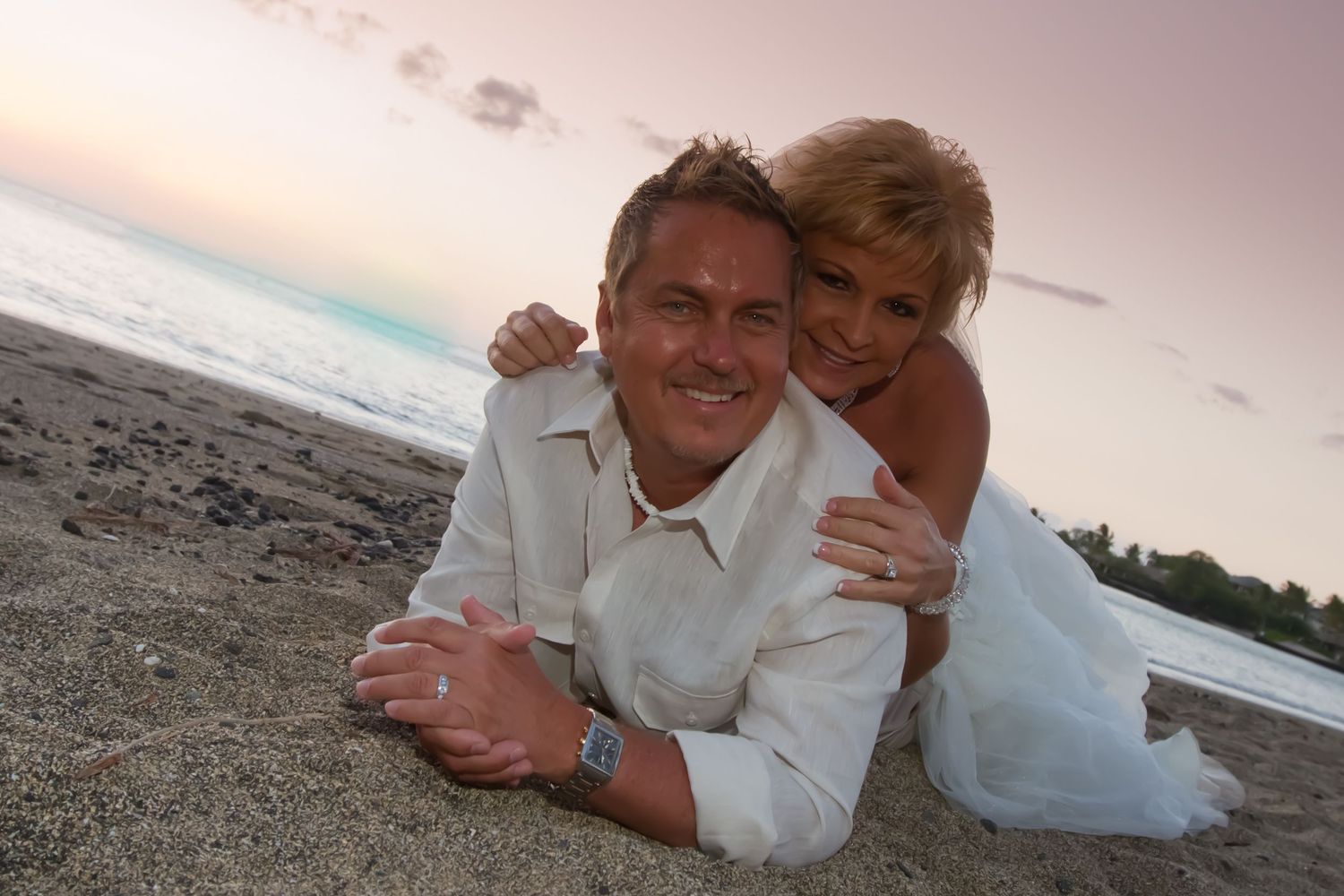 Romantic couple posing on the beach at sunset in white and beige attire.