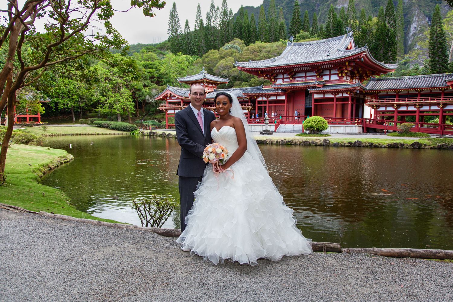Newlyweds pose by red Japanese Byodo-In temple and pond in tropical setting on Oahu, near Honolulu, Hawaii,