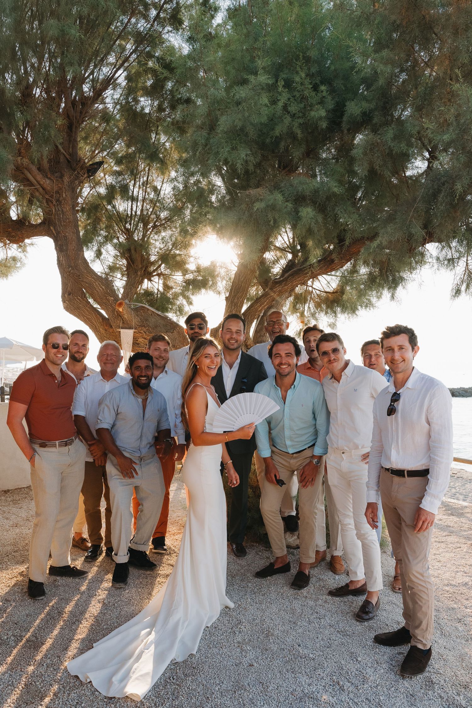 Wedding party gathers under a scenic tree during golden hour in Mediterranean destination wedding setting.