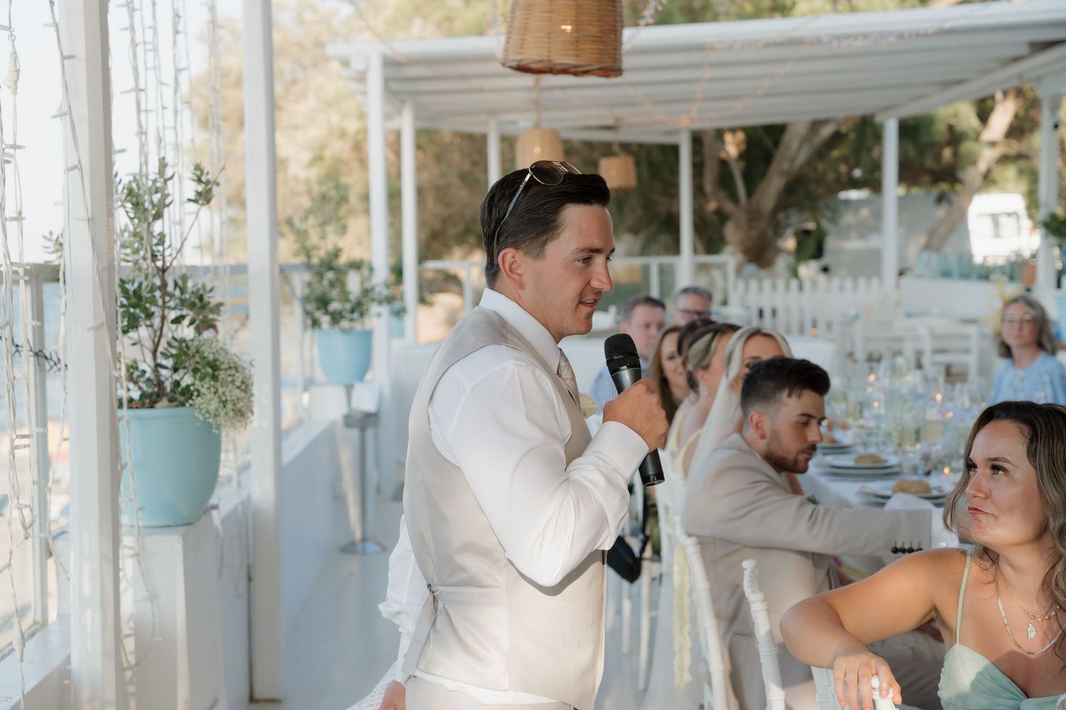 Wedding reception speech moment under white covered terrace with coastal views.