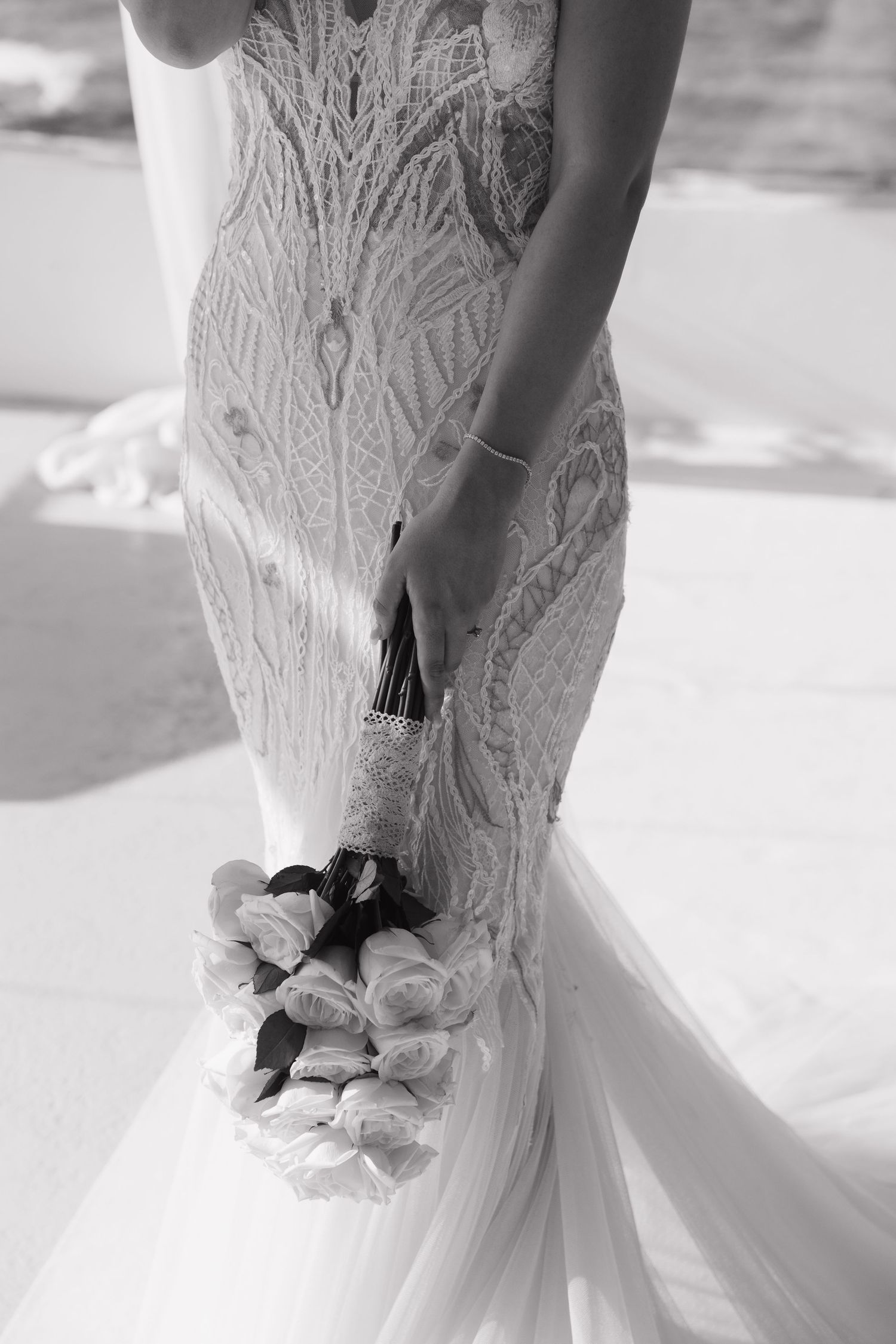 Close-up detail of an intricate lace wedding dress with floral appliques in black and white photography.