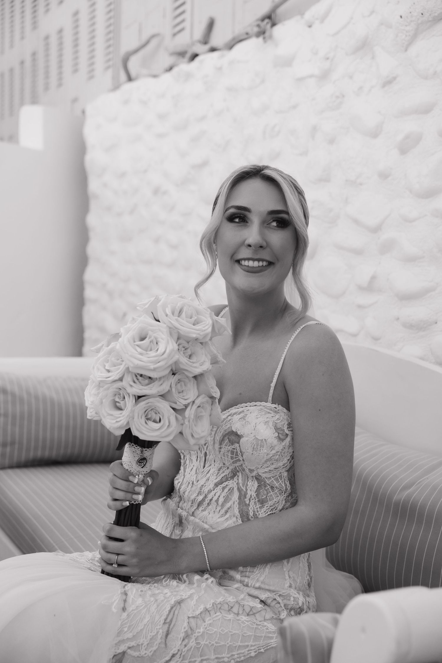 Black and white portrait of bride holding rose bouquet while sitting on couch.