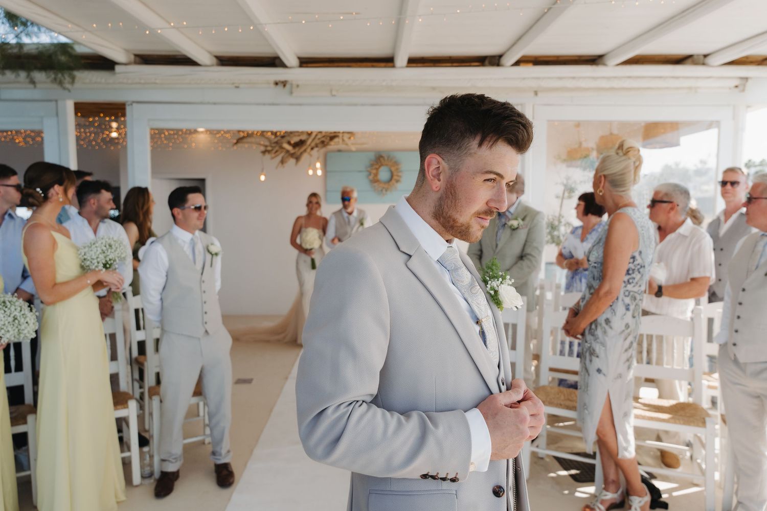 Groom in light gray suit reading during indoor ceremony.