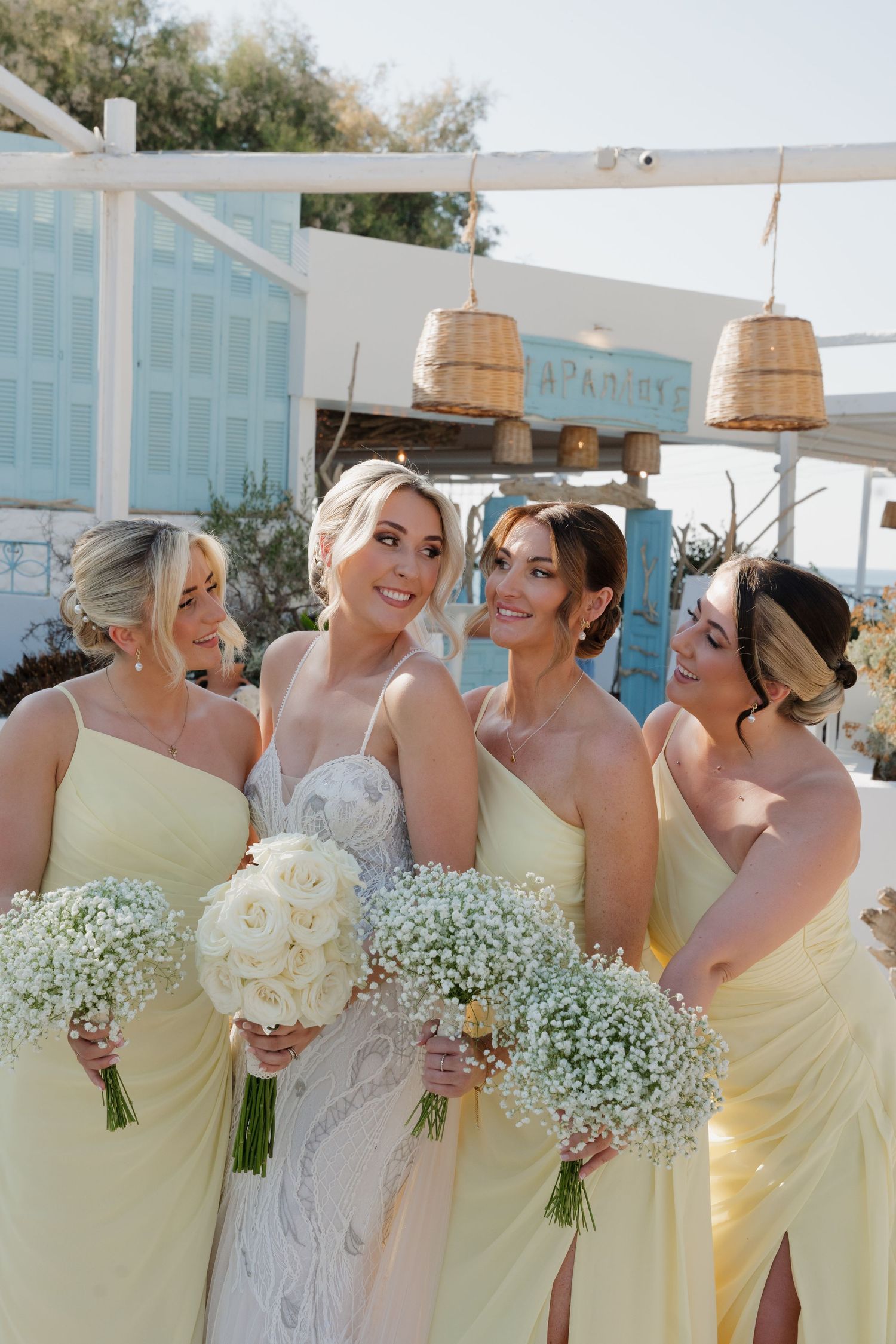 Bridesmaids in pale yellow dresses holding baby's breath bouquets under rustic hanging lanterns.