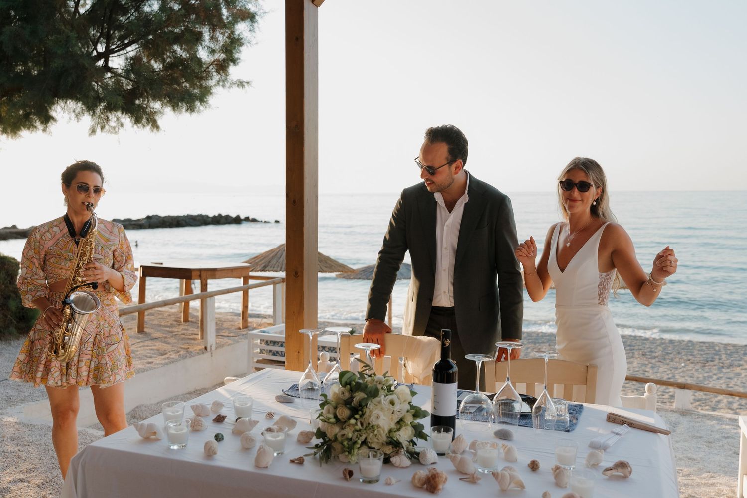 Wedding guests enjoying reception at oceanside table with floral centerpieces.