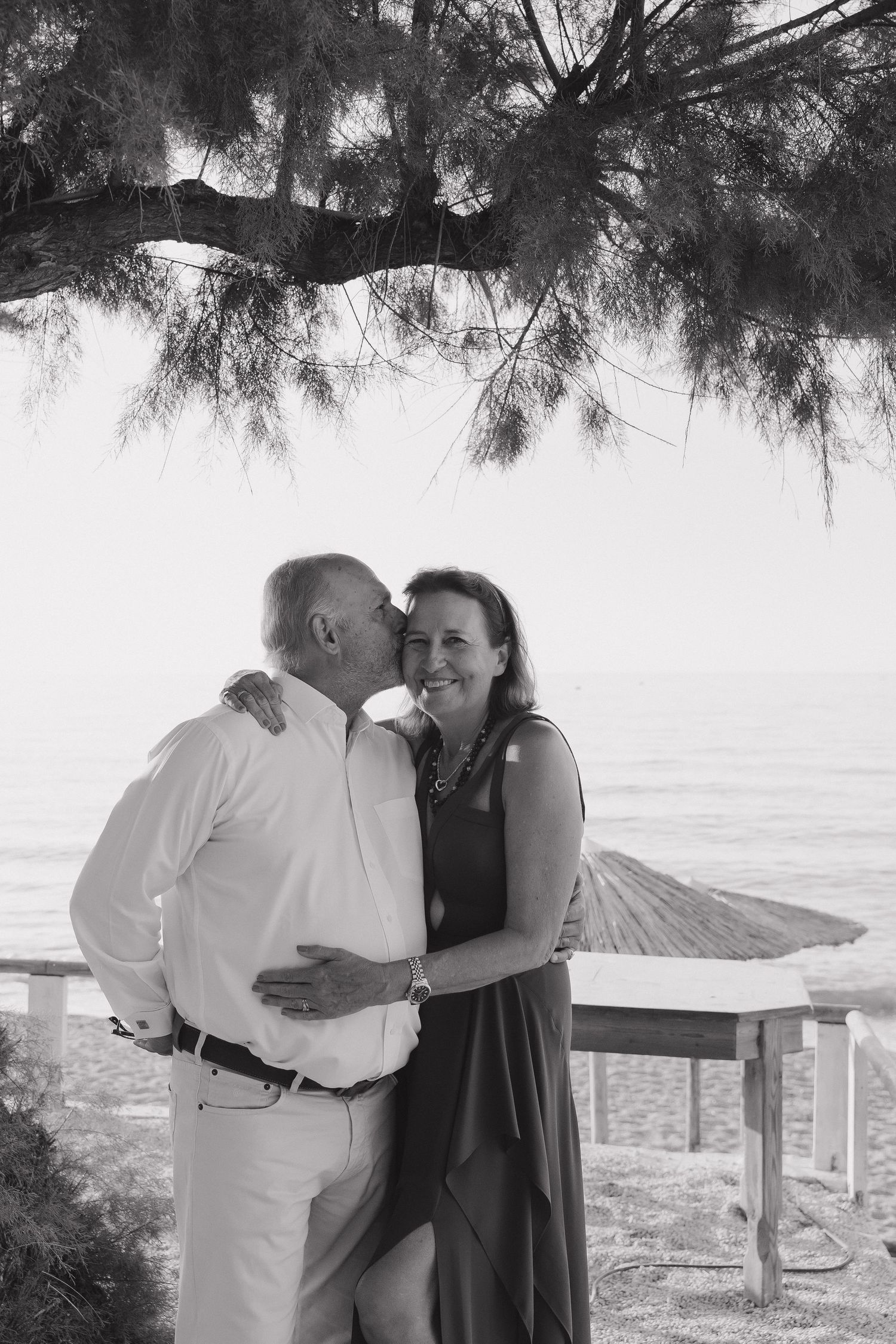 A romantic black and white moment shared between a couple beneath a pine tree branch with ocean views.