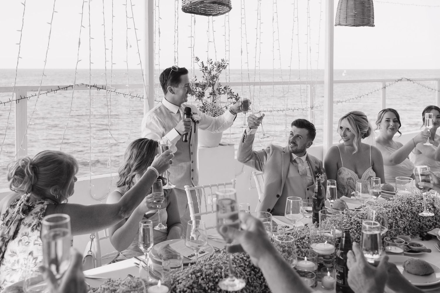 Black and white photo of wedding reception toast with guests raising glasses.