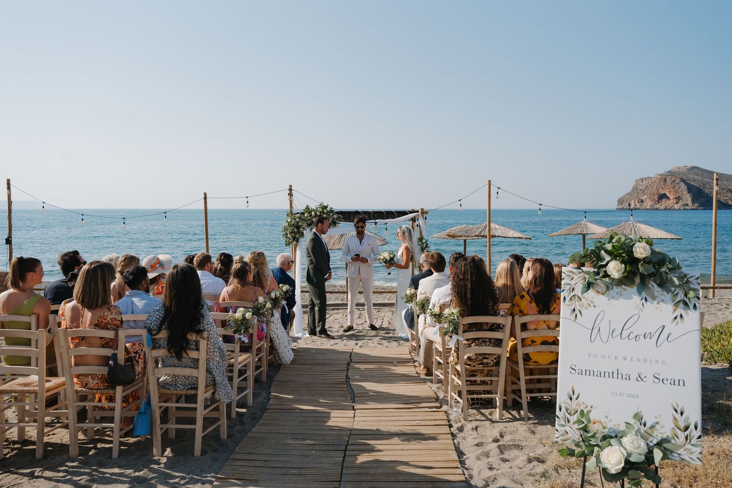 Oceanfront wedding ceremony setup with white chairs and floral arch against a coastal backdrop.