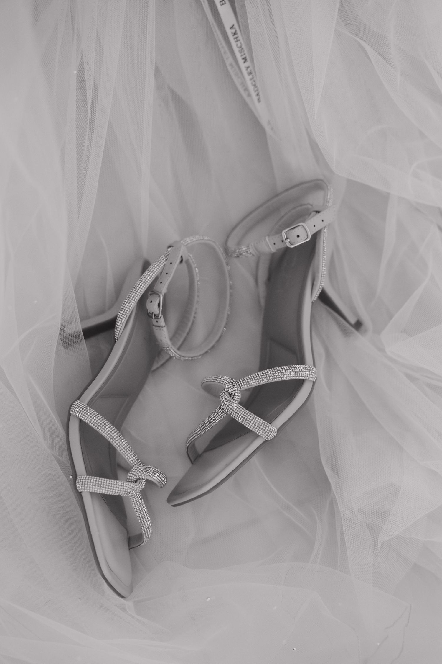 Elegant silver bridal heels with delicate straps laying on white tulle fabric.