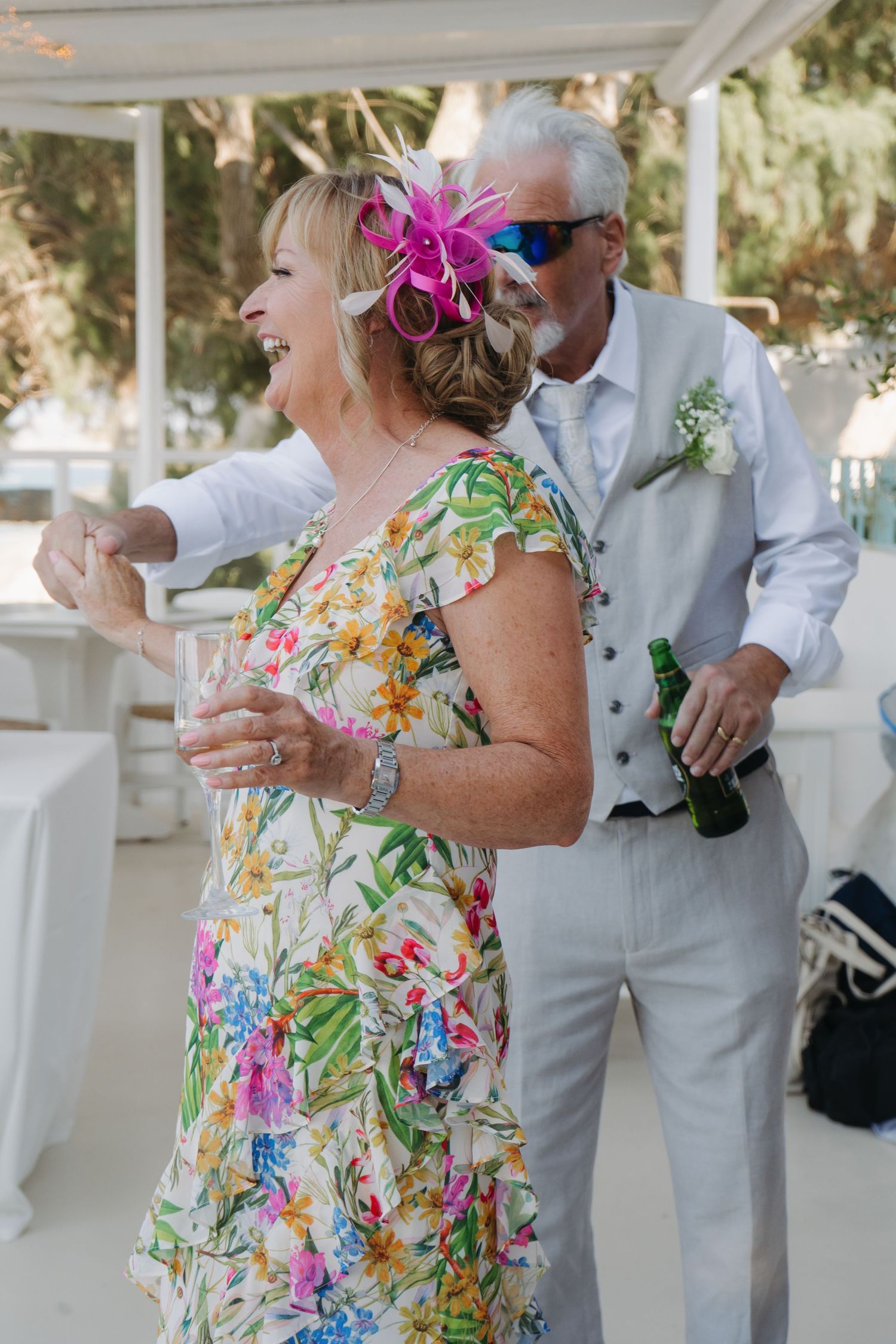 Couple dancing and laughing at wedding reception, wearing white and floral summer outfits.