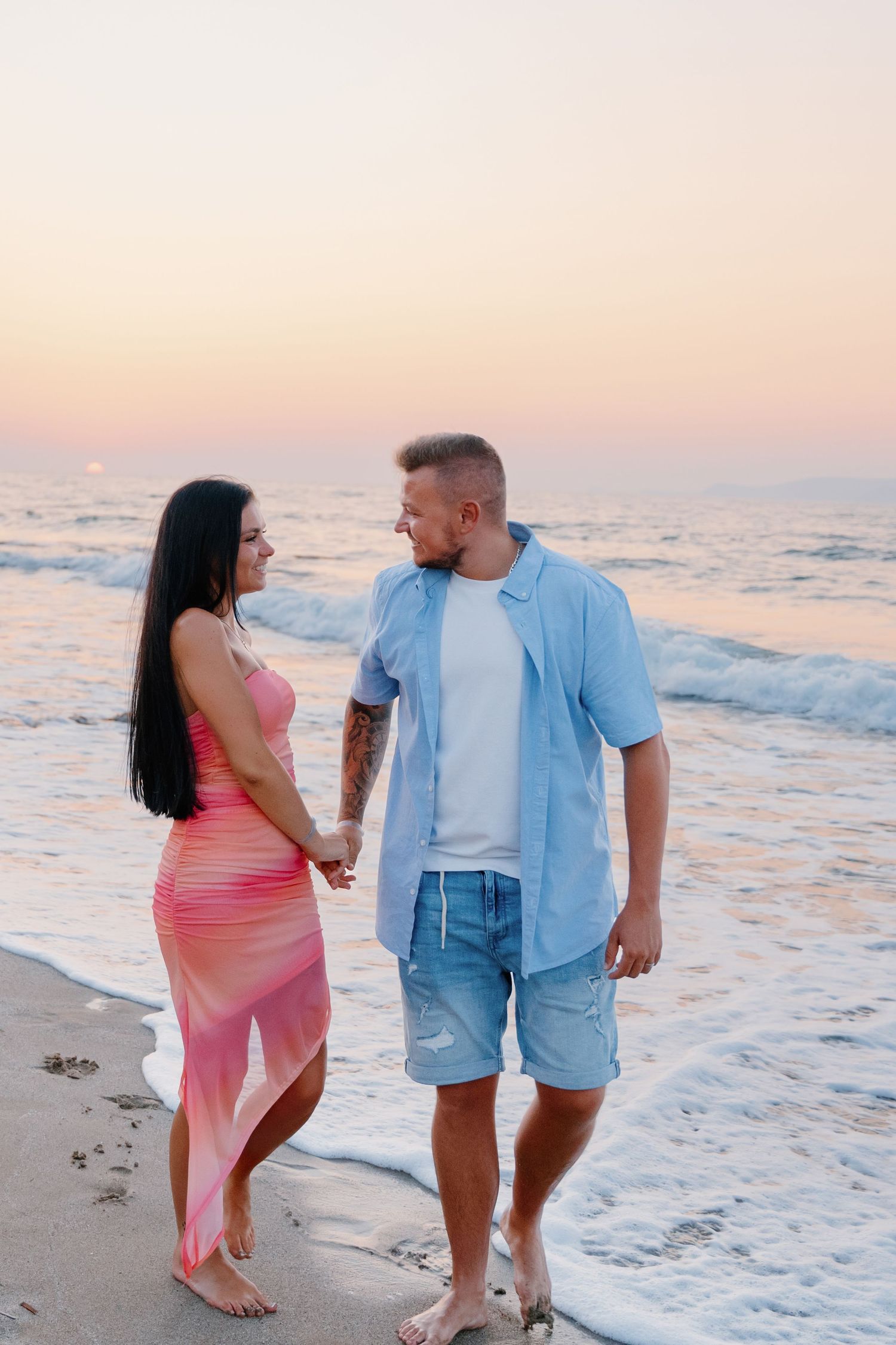 A couple holding hands while standing on the beach during golden hour.