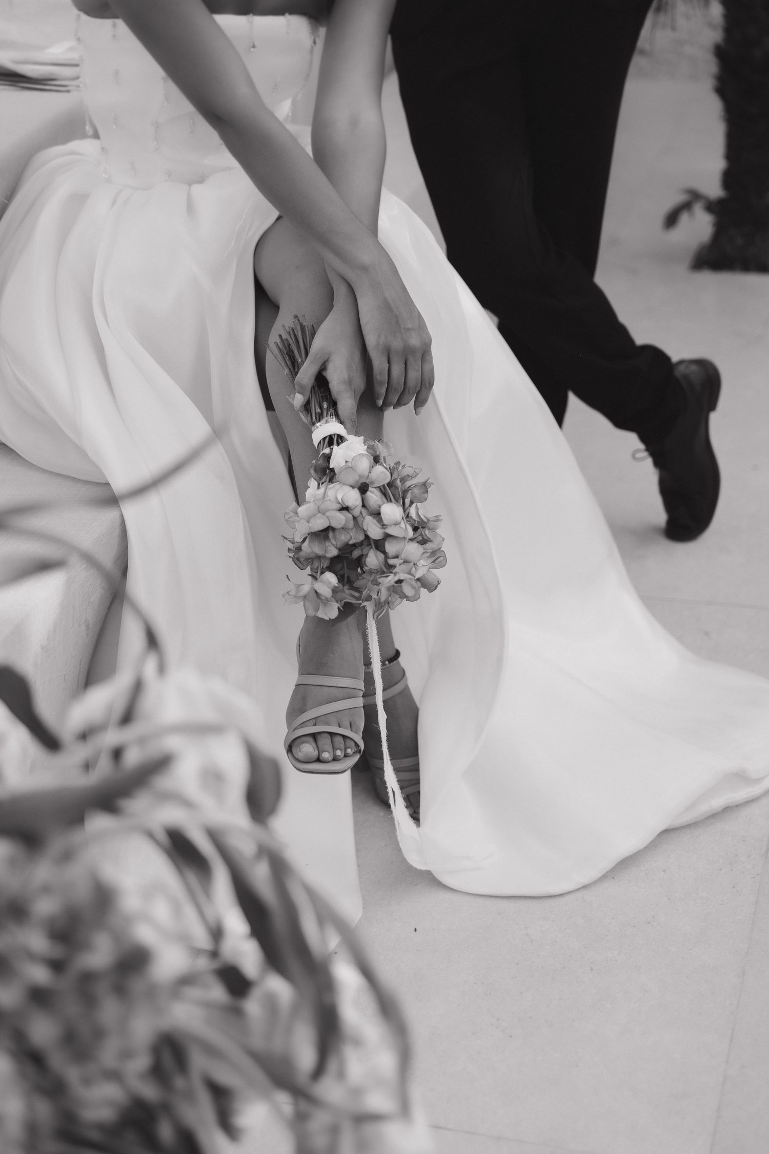Black and white detail shot of bride's ankle corsage with wedding dress and shoes.
