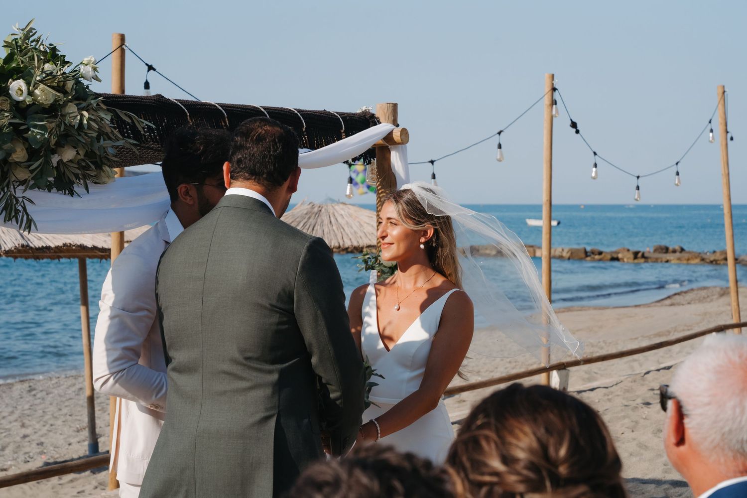 A seaside wedding ceremony with string lights overhead and the ocean visible in the background.
