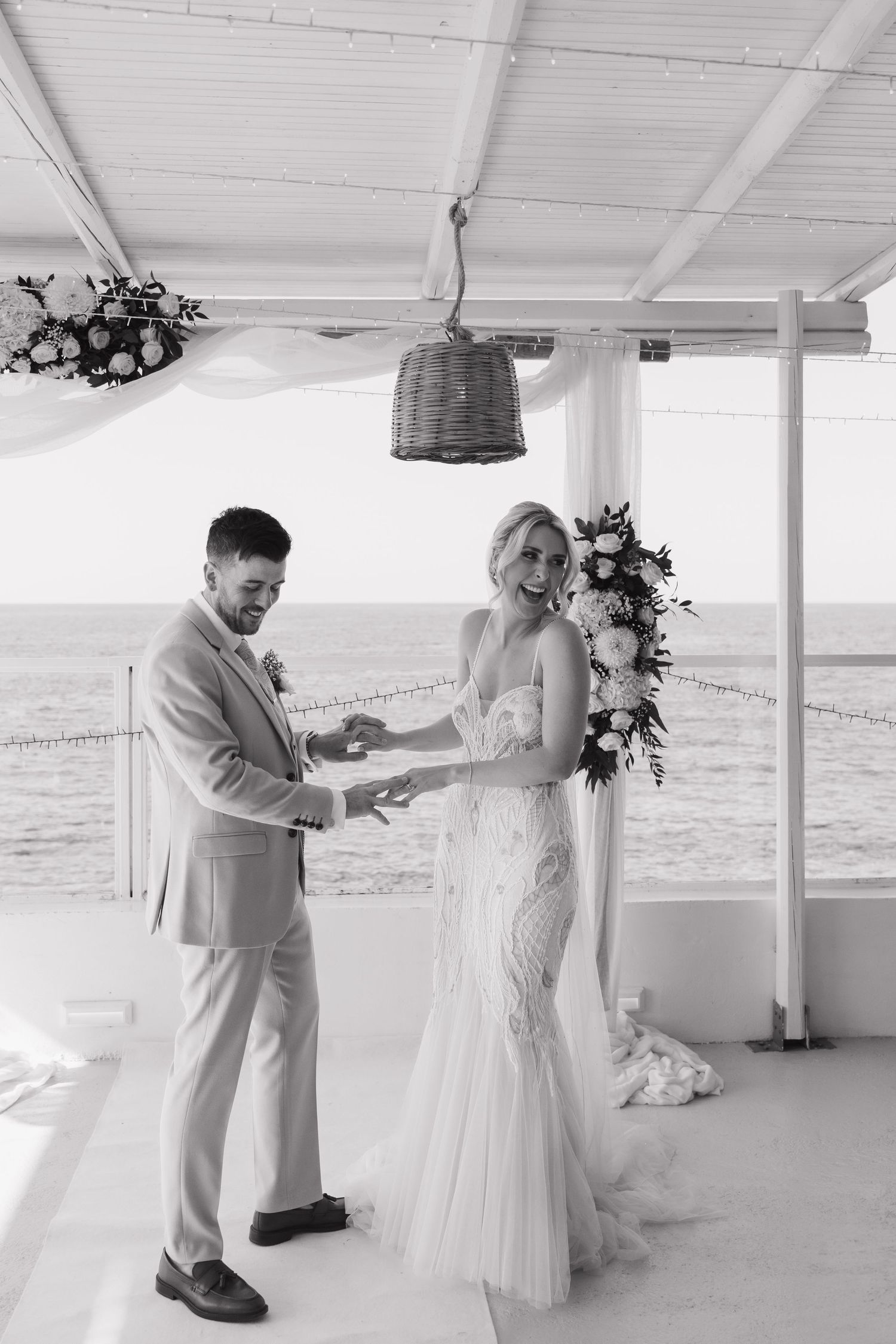 A couple shares a joyful moment during their oceanfront wedding ceremony in a covered seaside venue.