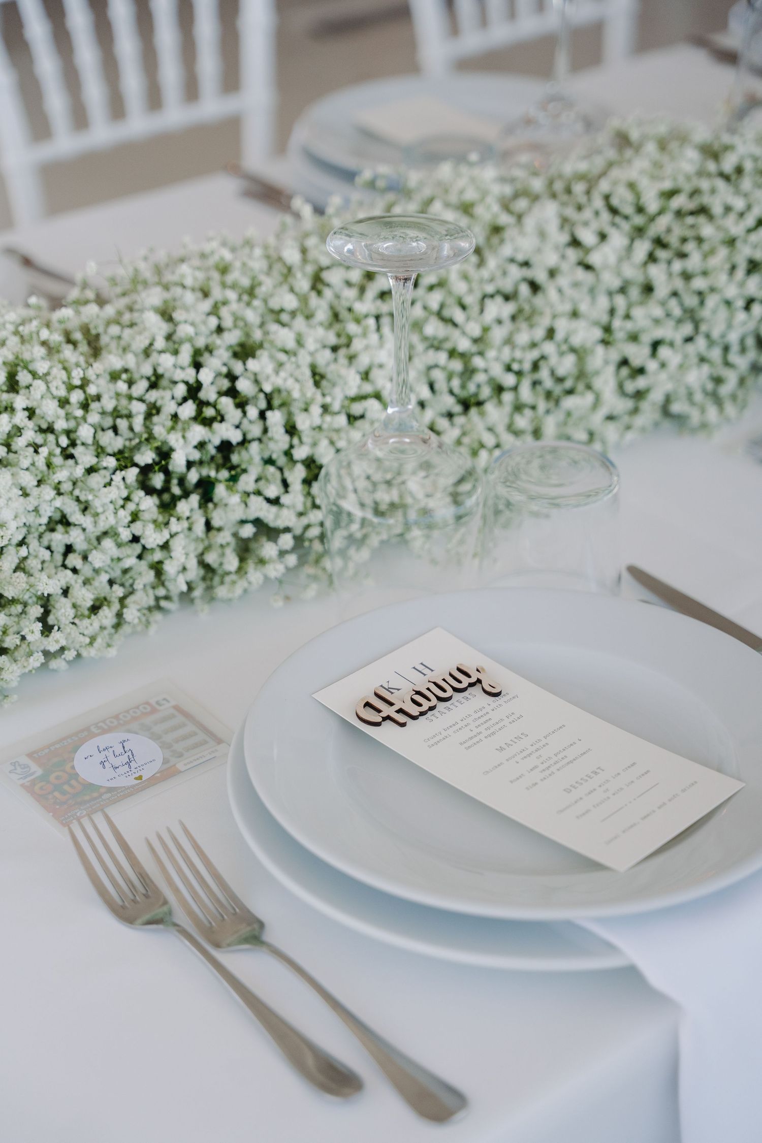 White place setting with baby's breath floral runner and menu card on white plates.