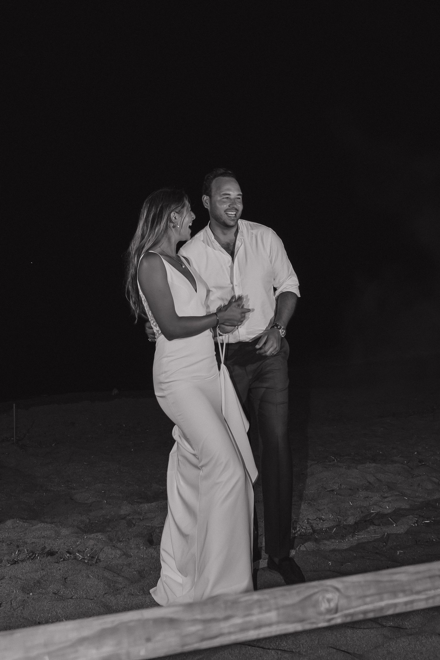 A couple shares an intimate black and white moment on their wedding night by the ocean.
