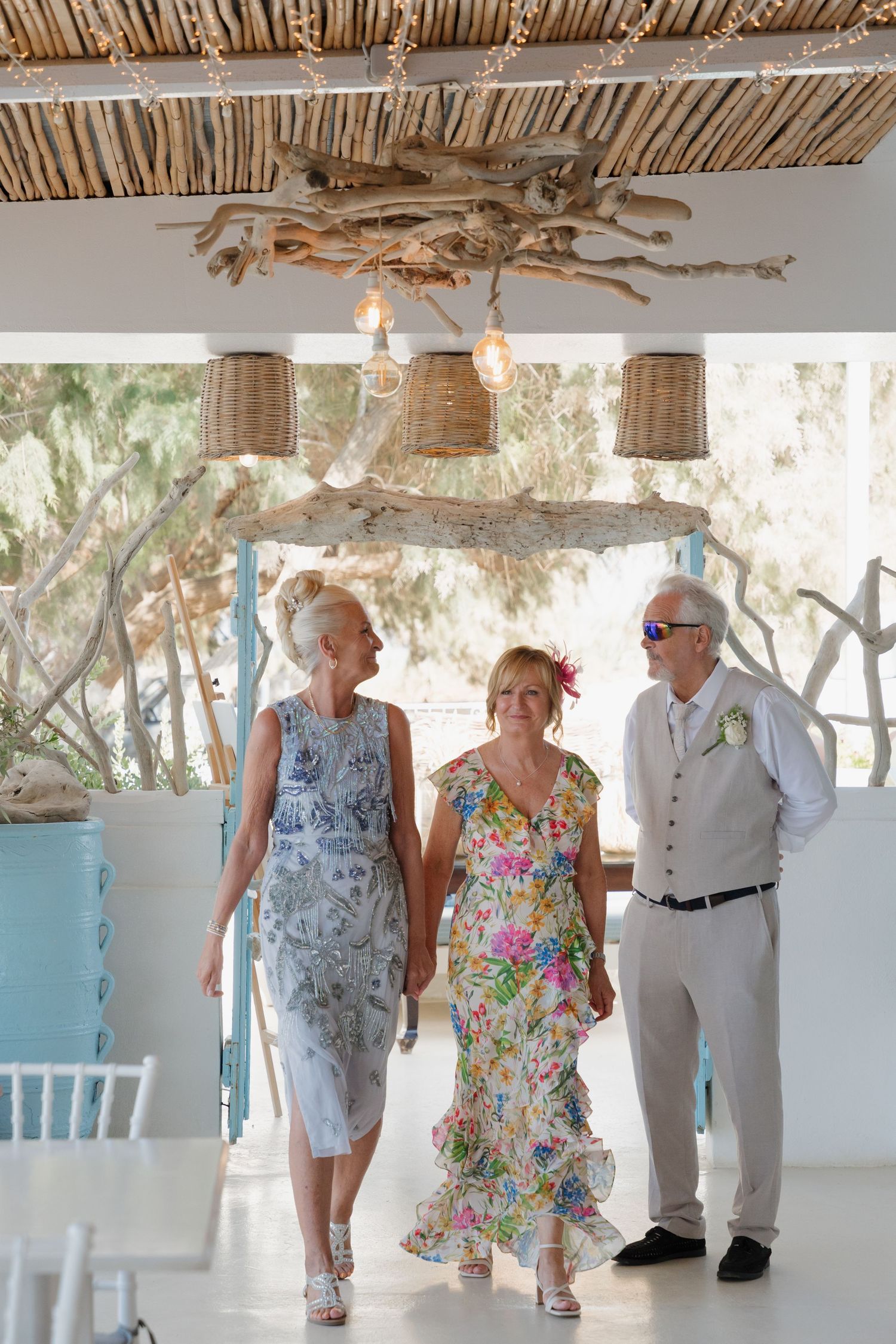 Three wedding guests walking together under rustic bamboo ceiling with hanging basket lights.