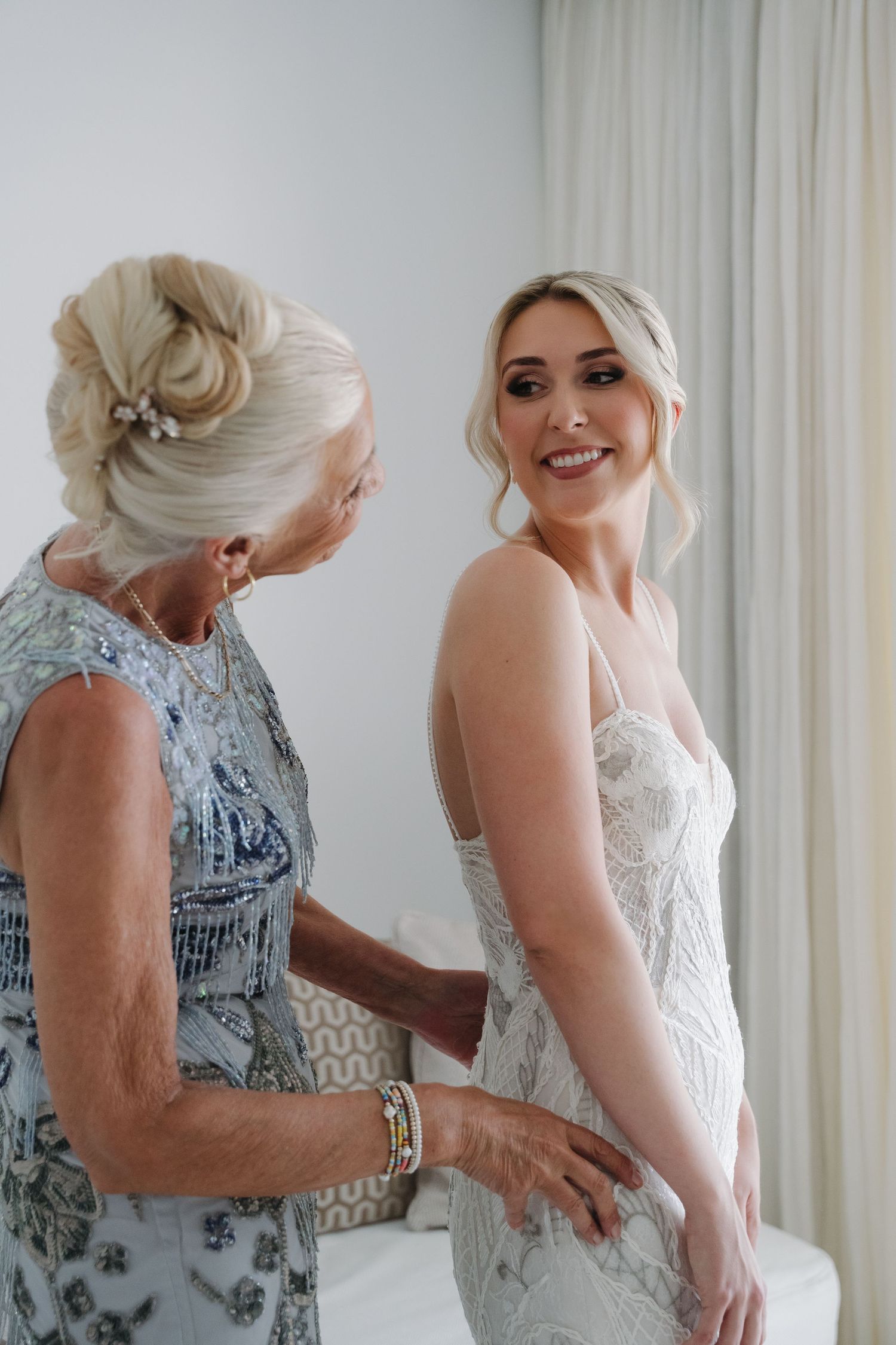 Elegant wedding dress fitting scene with lace details in bright white room.
