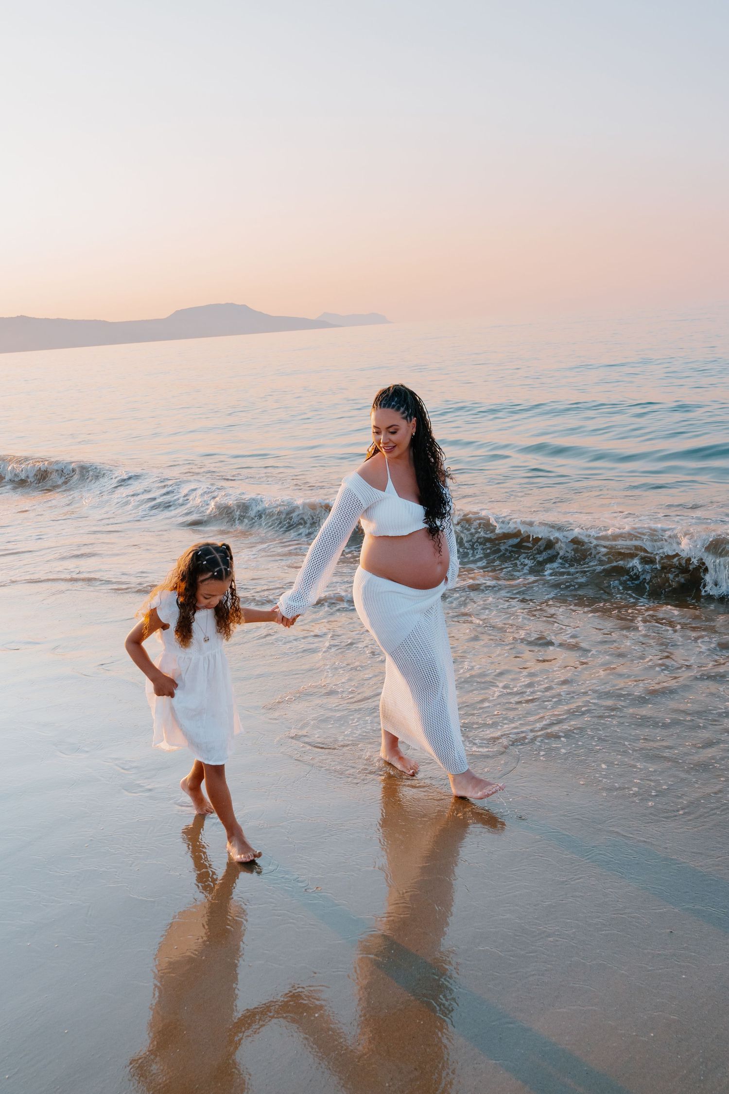 A heartwarming beach scene of an expectant mother and child walking along the shoreline at sunset.