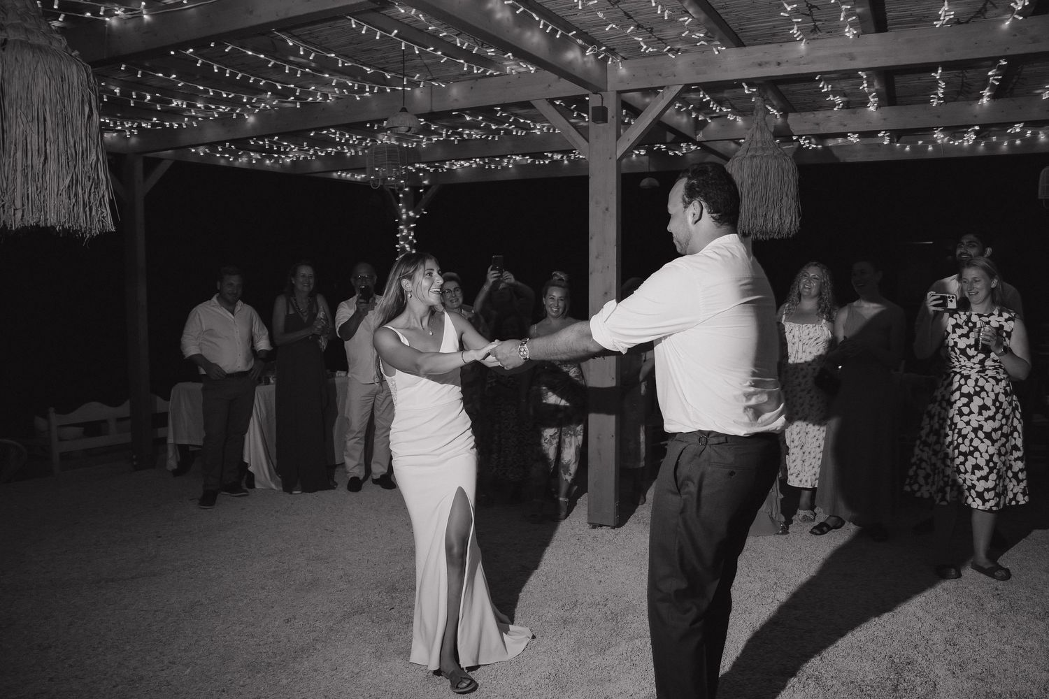 Dancing under twinkling lights at outdoor reception in black and white.