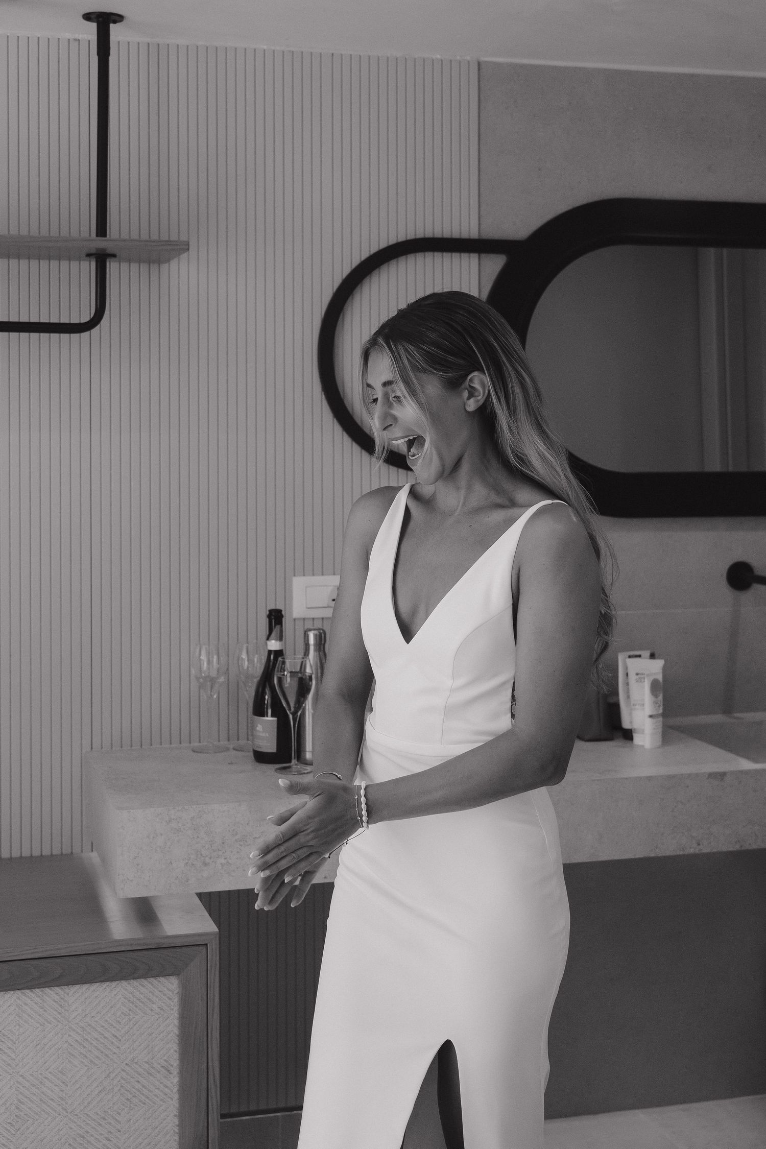 A candid moment showing a person in a white sleeveless dress laughing in an indoor setting.